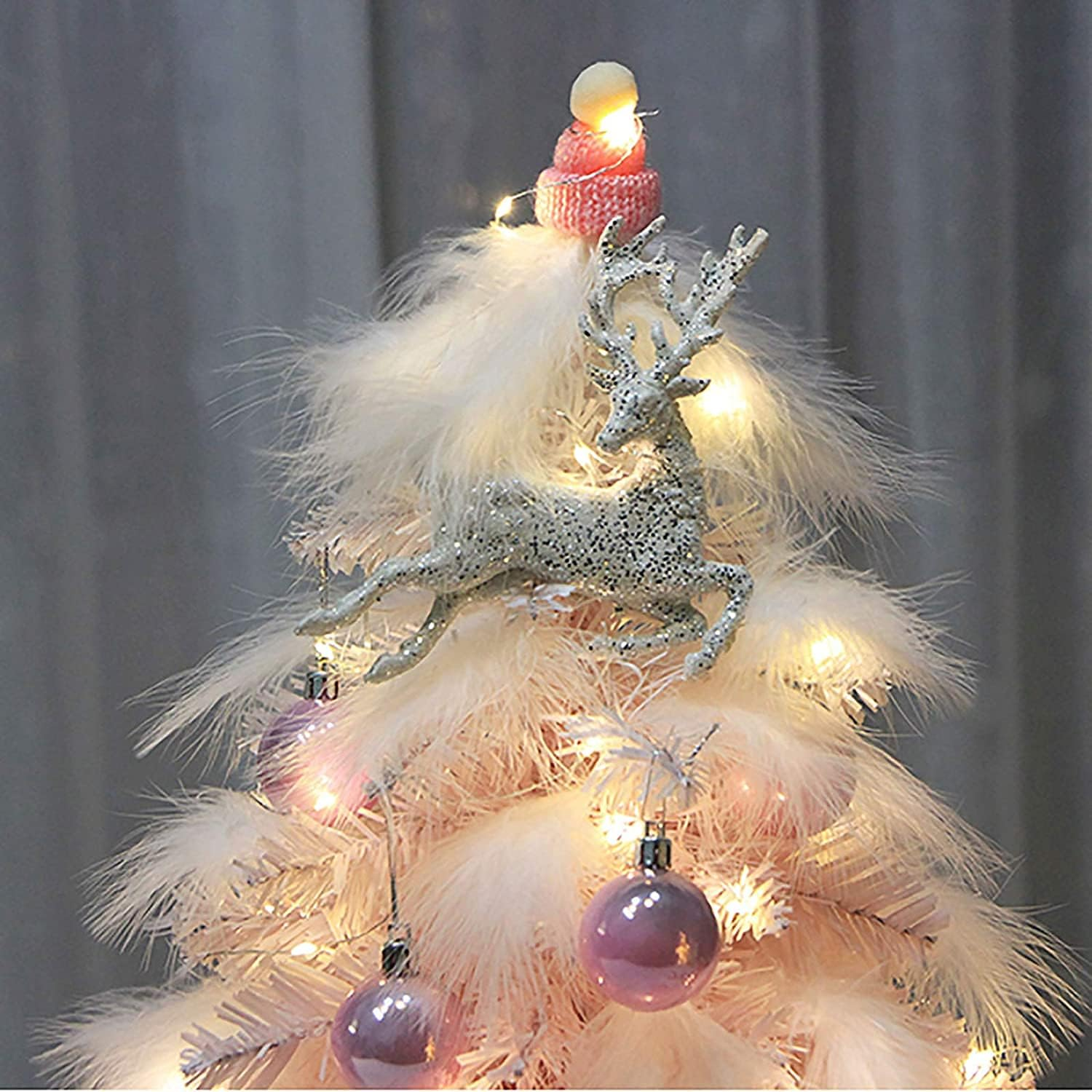 Ein dekorativer Weihnachtsbaum mit rosa Federn, Ornamenten und einem silbernen Rentier-Topper.