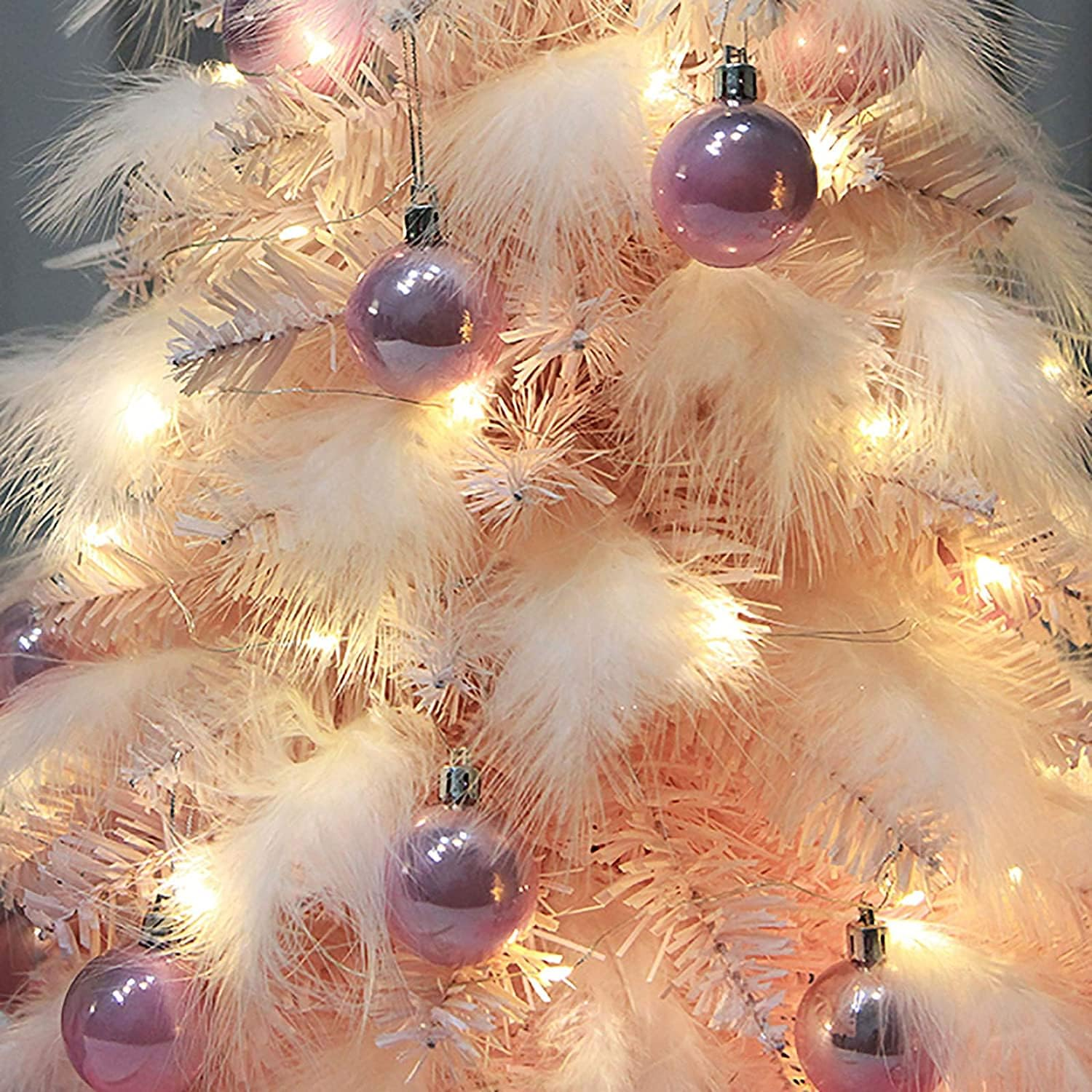 Nahaufnahme eines Weihnachtsbaums mit rosa Ornamenten und weißen Federn.