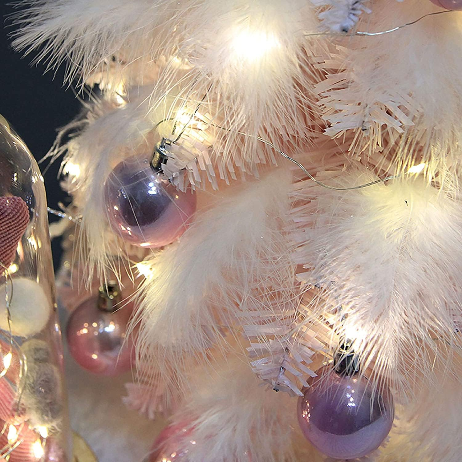 Weihnachtsbaum mit weißen Federn, dekoriert mit rosa Ornamenten und Lichtern, Nahaufnahme.