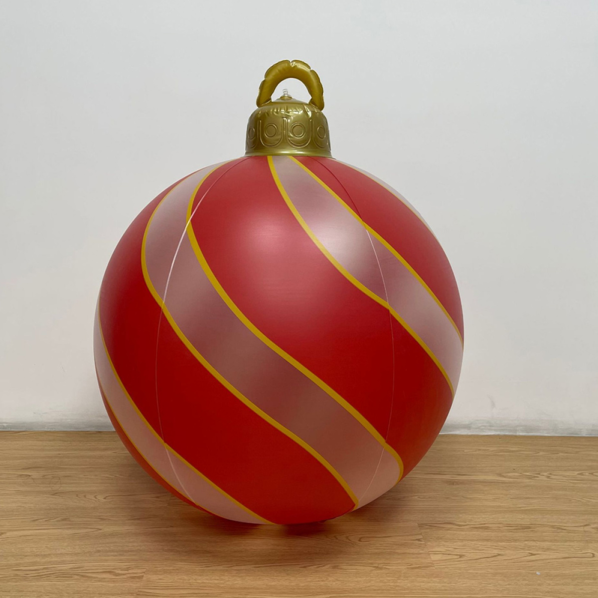 Große rote Weihnachtskugel mit weißen und gelben Streifen auf Holzboden, im Hintergrund eine weiße Wand.