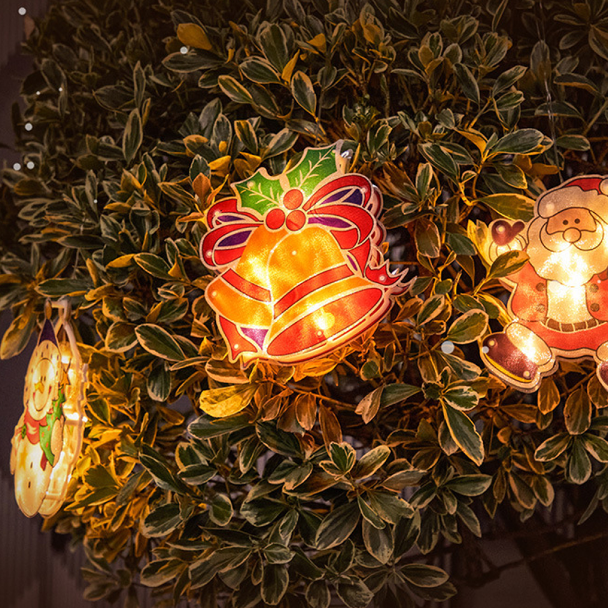 Weihnachtsbeleuchtung an einem Busch, mit Glocke, Weihnachtsmann und Schneemann. Warmes, gelbes Licht.