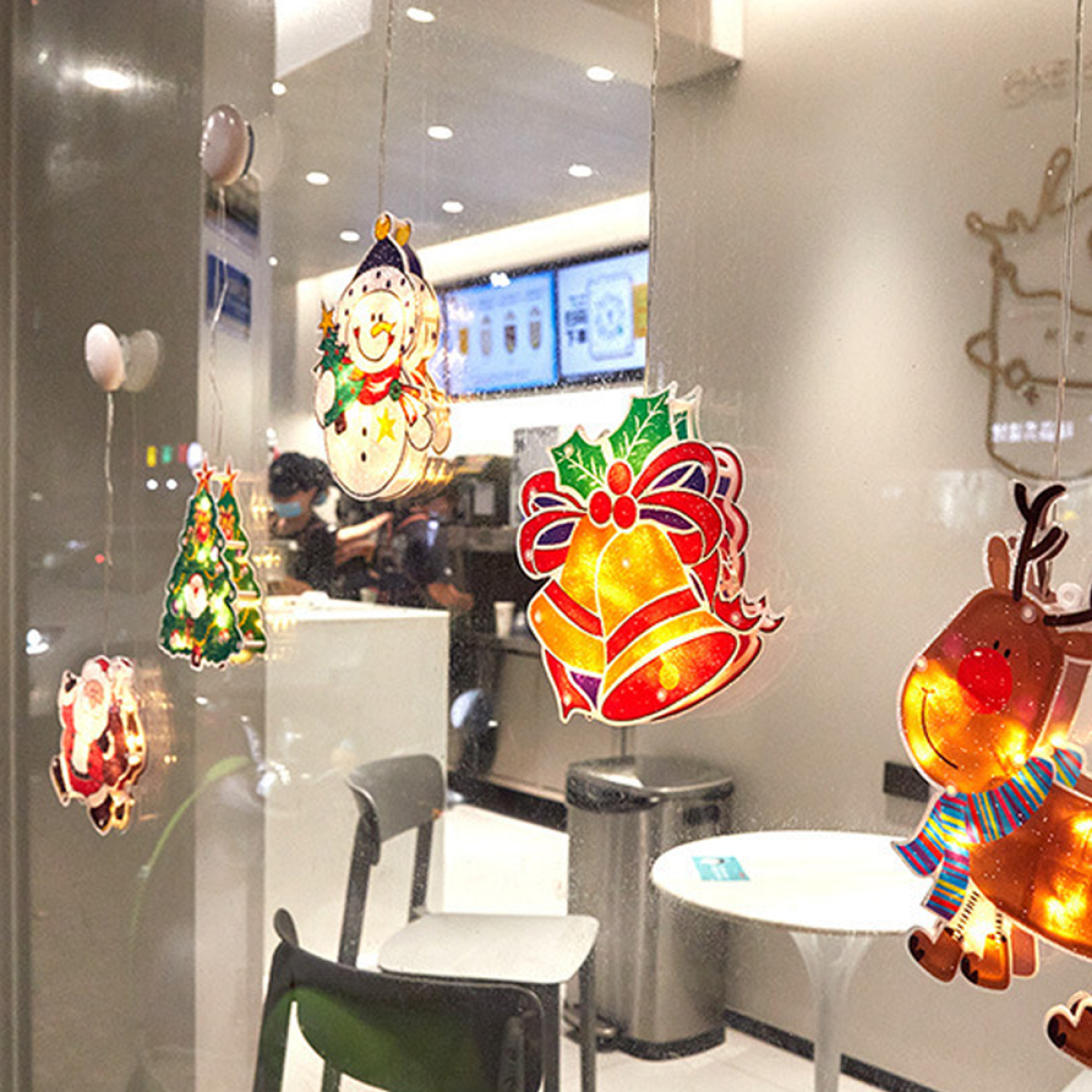 Weihnachts-Fensterdekorationen mit Schneemann, Baum, Glocken und Rentier, in einem Geschäft.