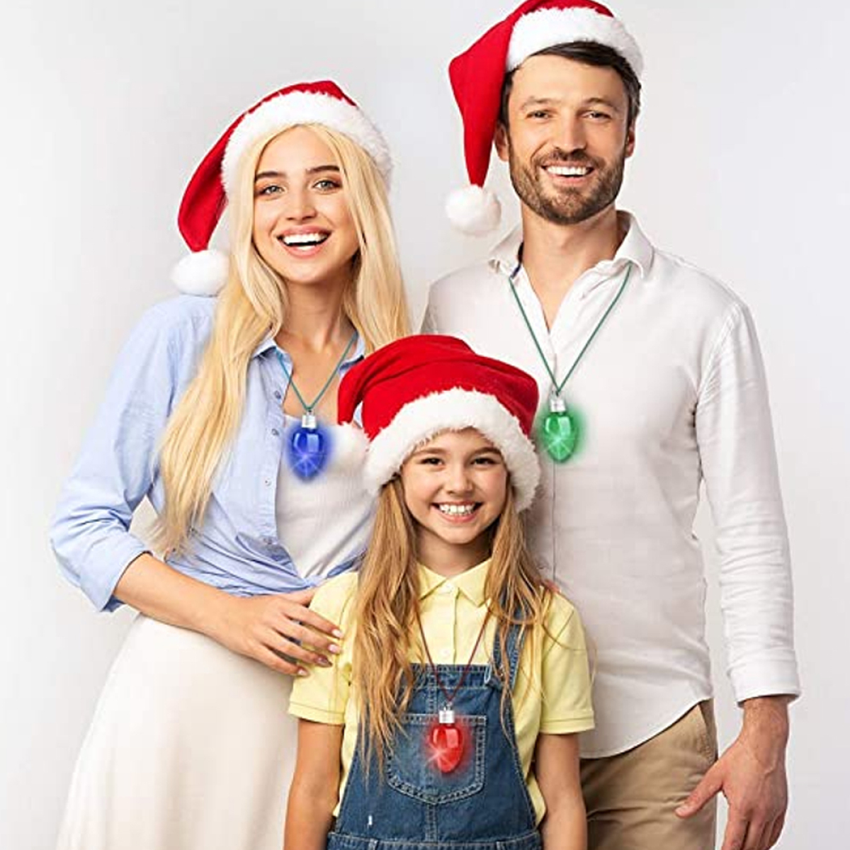 Eine Familie, die Weihnachtslichterketten und Weihnachtsmützen trägt und lächelt.