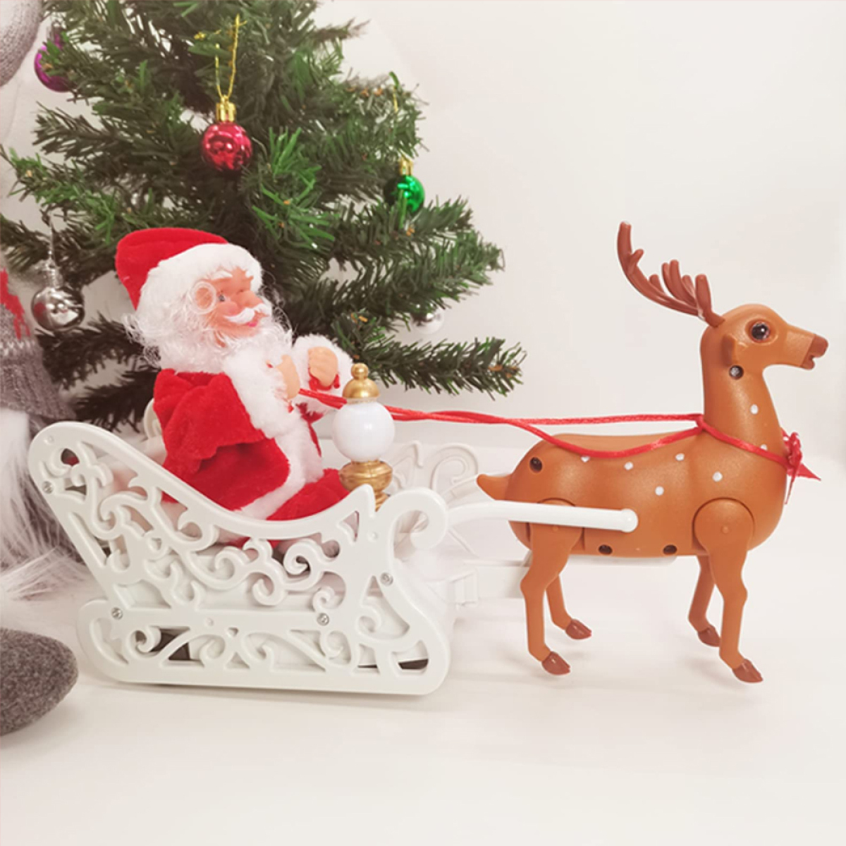 Weihnachtsmann in einem Schlitten, gezogen von einem Rentier vor einem kleinen Weihnachtsbaum.