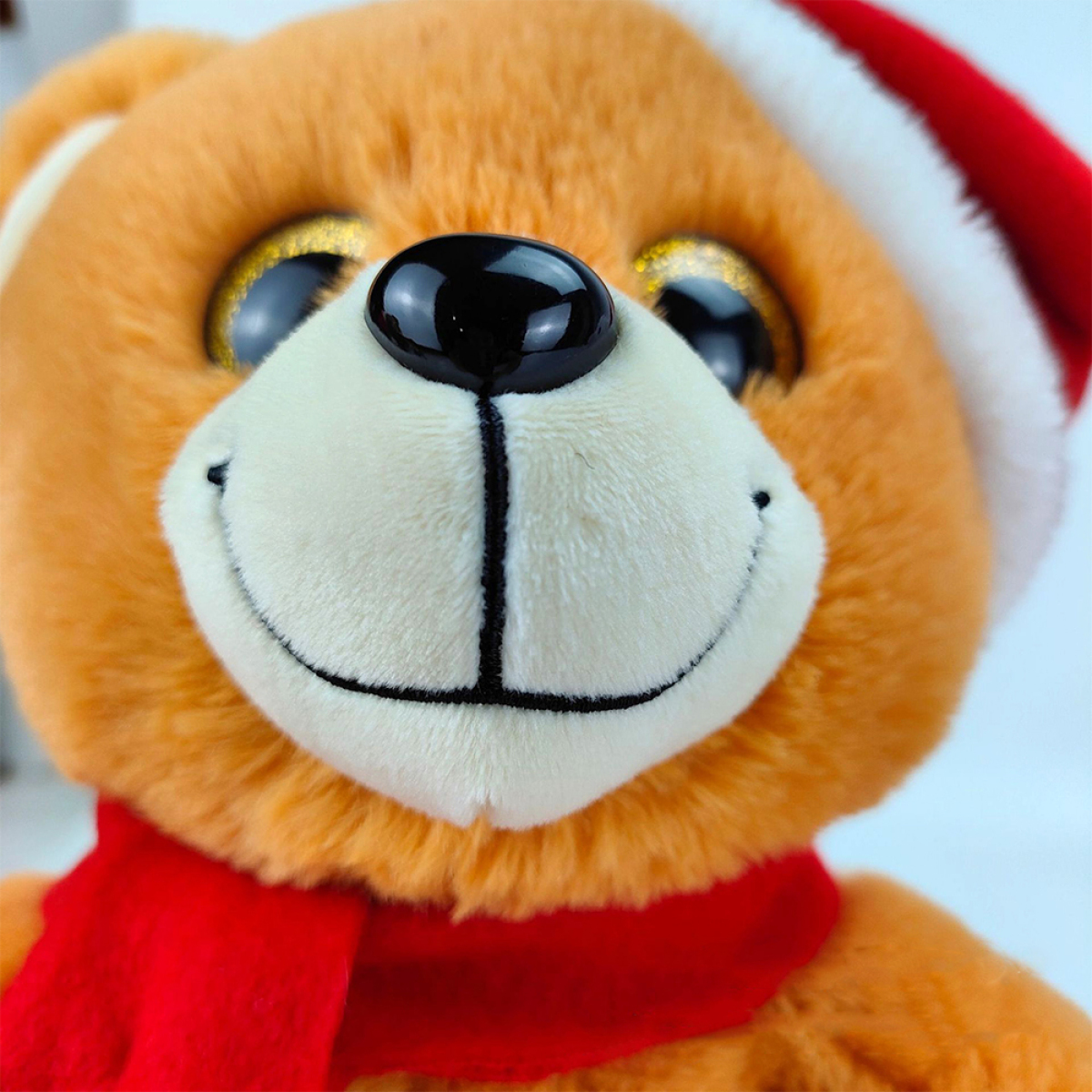 Nahaufnahme eines Teddybären mit Weihnachtsmütze und rotem Schal, lächelnd.