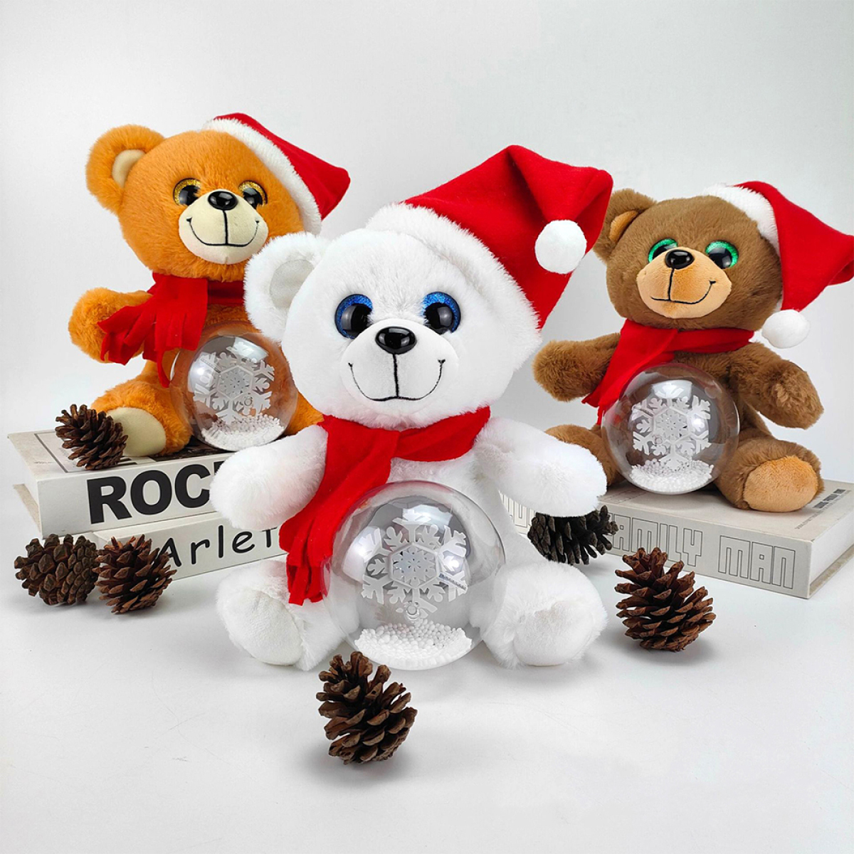Drei Teddybären mit Weihnachtsmützen und Schneekugeln auf weißer Oberfläche.