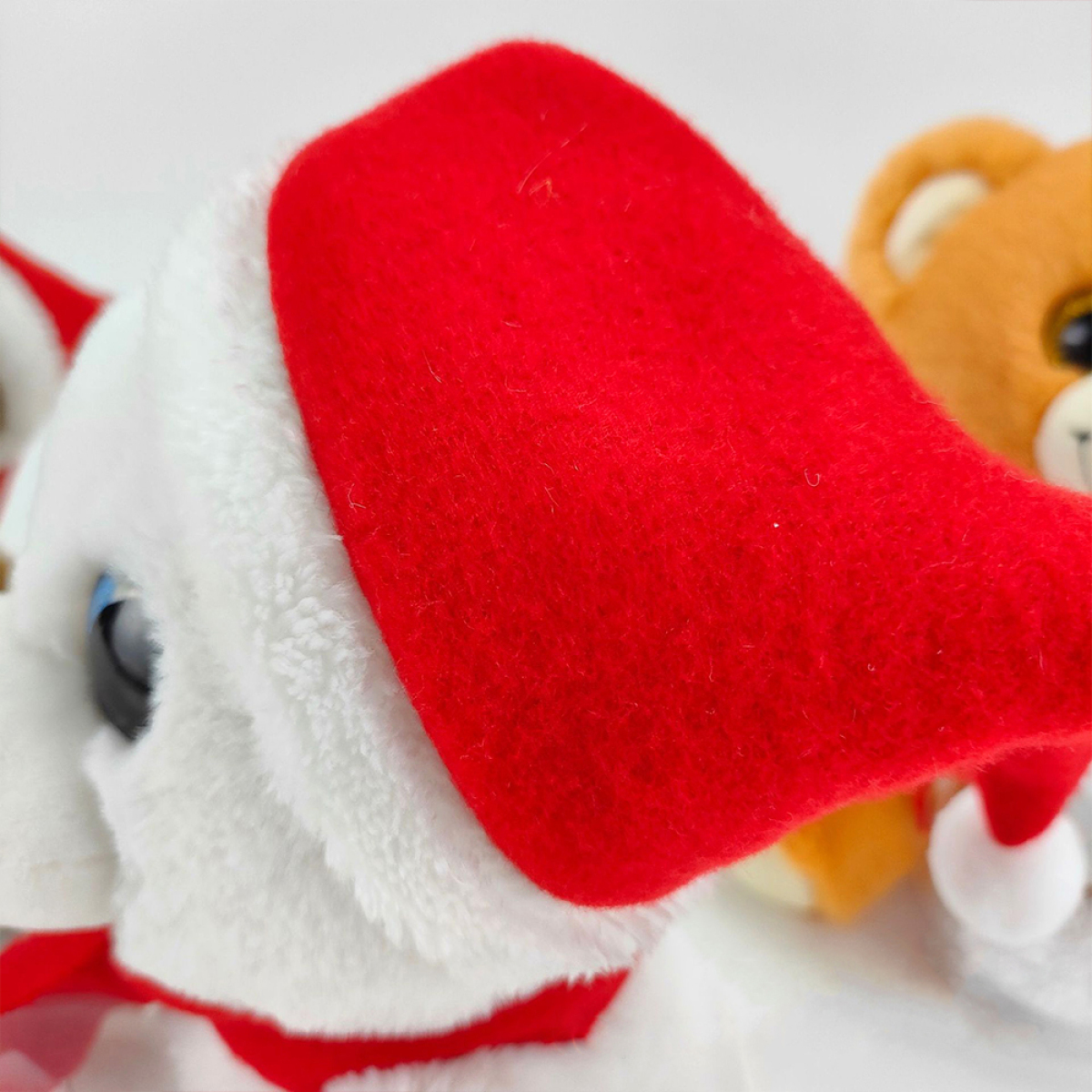 Nahaufnahme eines weißen Stofftiers mit Weihnachtsmütze, Teddybär im Hintergrund.