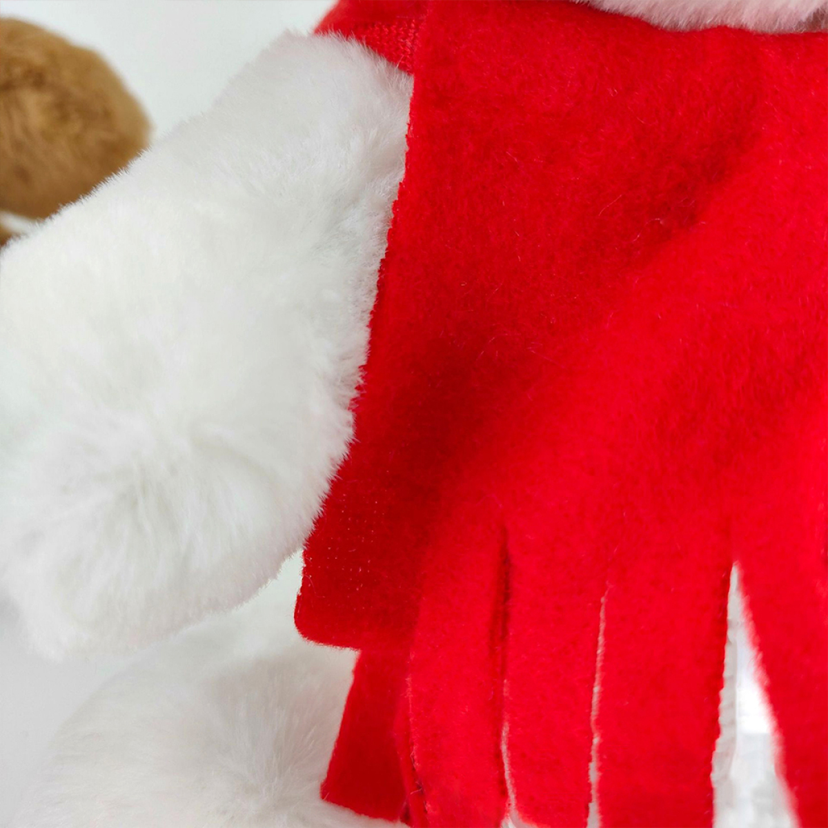 Nahaufnahme eines Weihnachts-Plüschartikels. Ein roter Schal mit weißem, flauschigem Rand. Ein braunes Plüschartikel im Hintergrund.