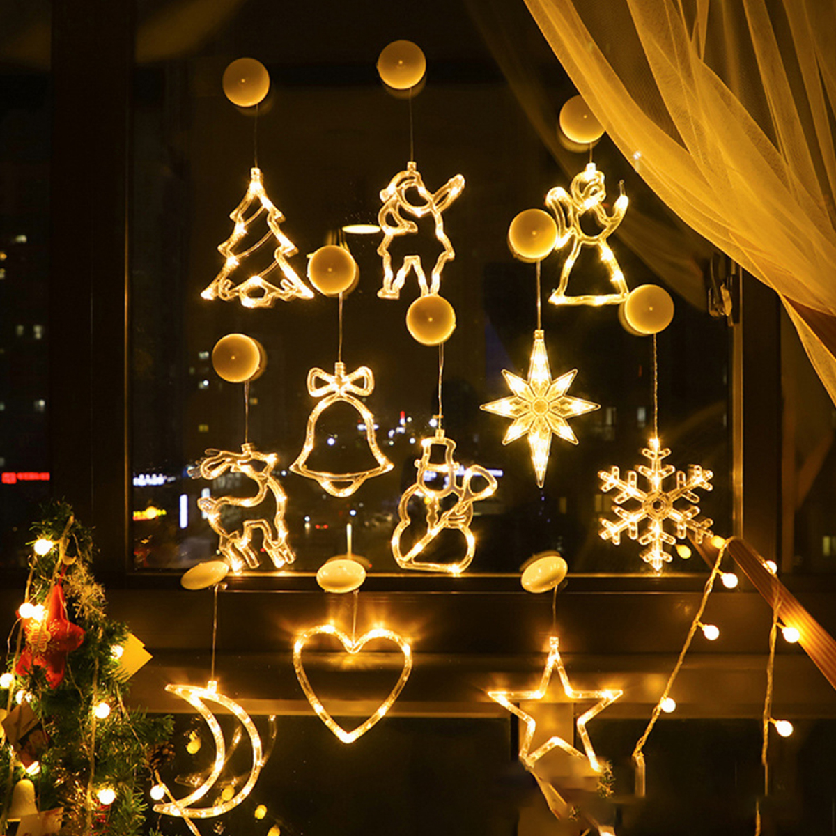 Fenster mit Weihnachtsbeleuchtung in verschiedenen Formen. Baum, Rentier, Glocke, Schneemann, Stern und Engel sind sichtbar.