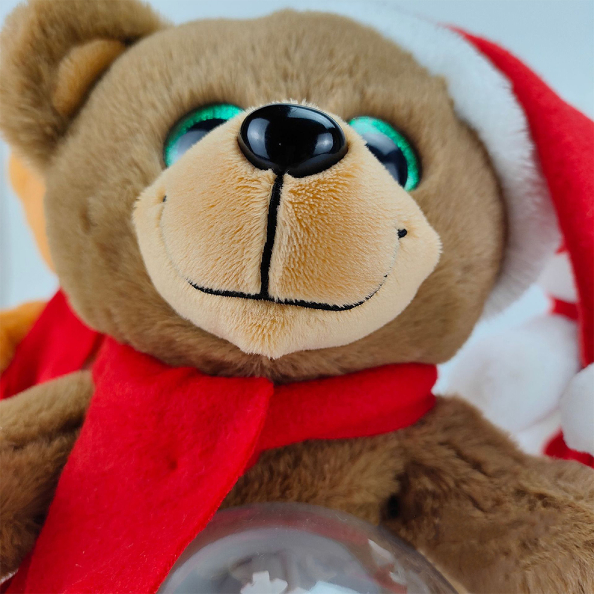 Brauner Teddybär mit Weihnachtsmütze und Schal, hält Glaskugel mit Schnee.