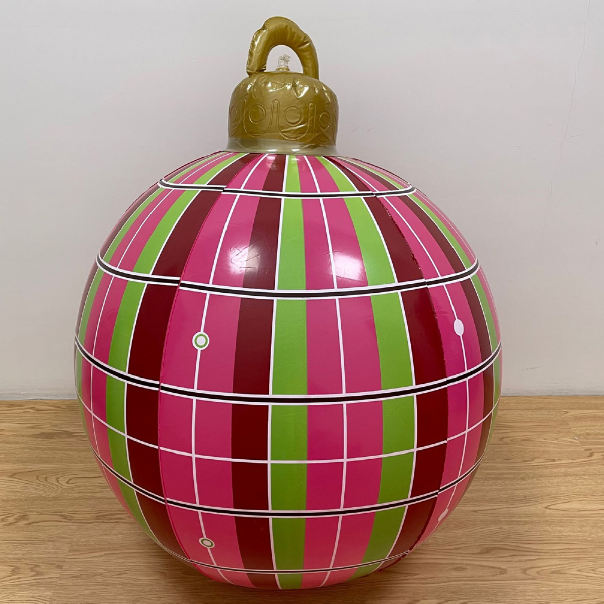 Große, bunte Weihnachtsornament mit rosa, grünen und roten Streifen auf Holzboden.