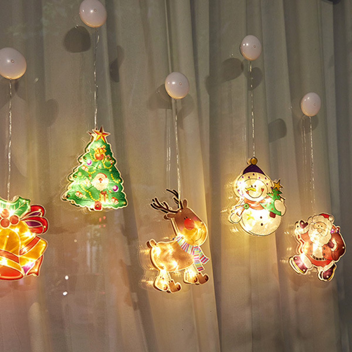 Weihnachtsbeleuchtung hängt an einem Fenster. Dekorationen umfassen einen Baum, Rentiere, Schneemann und Santa.