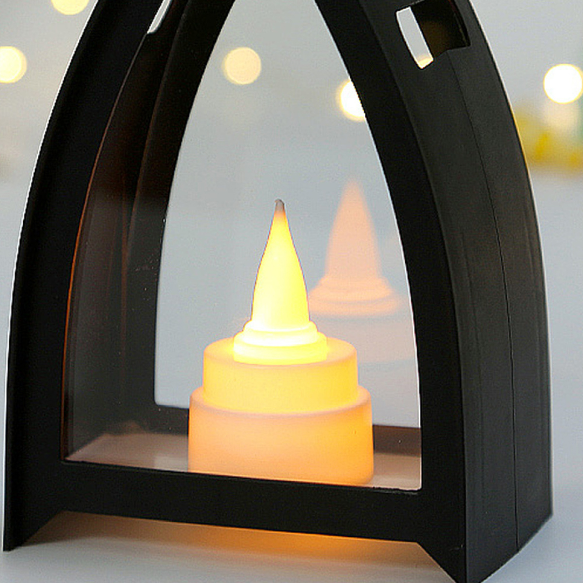 Schwarzer Laternen-Kerzenhalter mit einer brennenden, gelb-orangen LED-Kerze im Inneren.