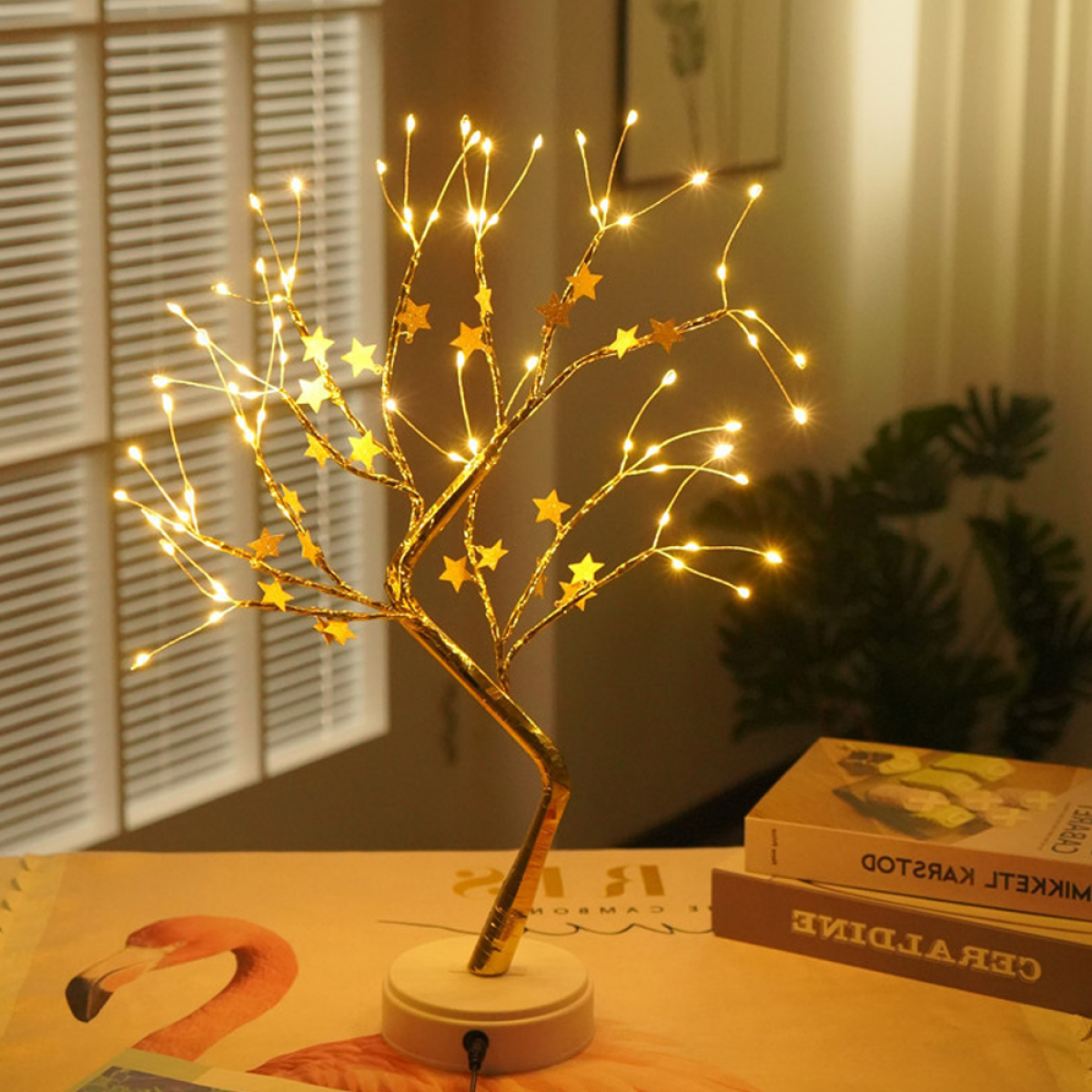 Ein dekorativer Baum mit Lichtern und Sternen auf einem Schreibtisch mit Büchern.