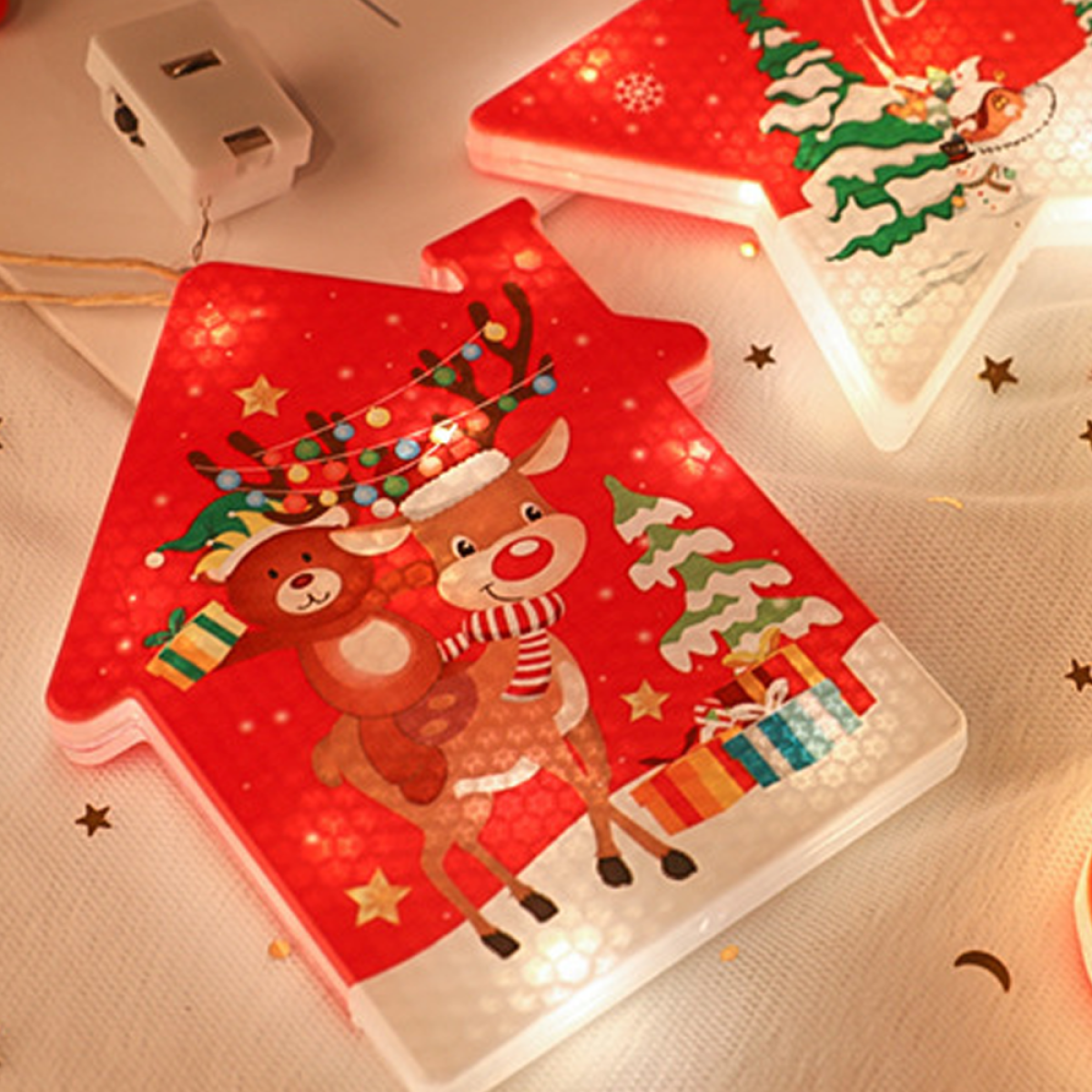 Hausförmige Weihnachtsbeleuchtung mit Rentier- und Bärdesign, rot, mit weißen Lichtern und Sternen. Der Hintergrund ist weiß.