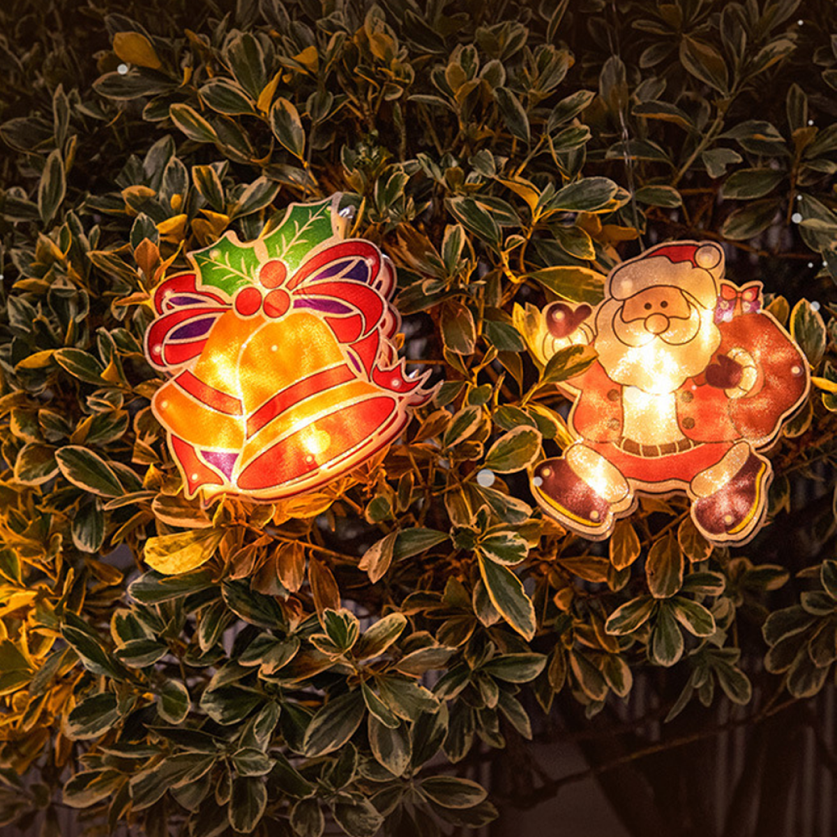 Weihnachtsbeleuchtung: Glocken- und Weihnachtsmann-förmige Lichter im Laub.