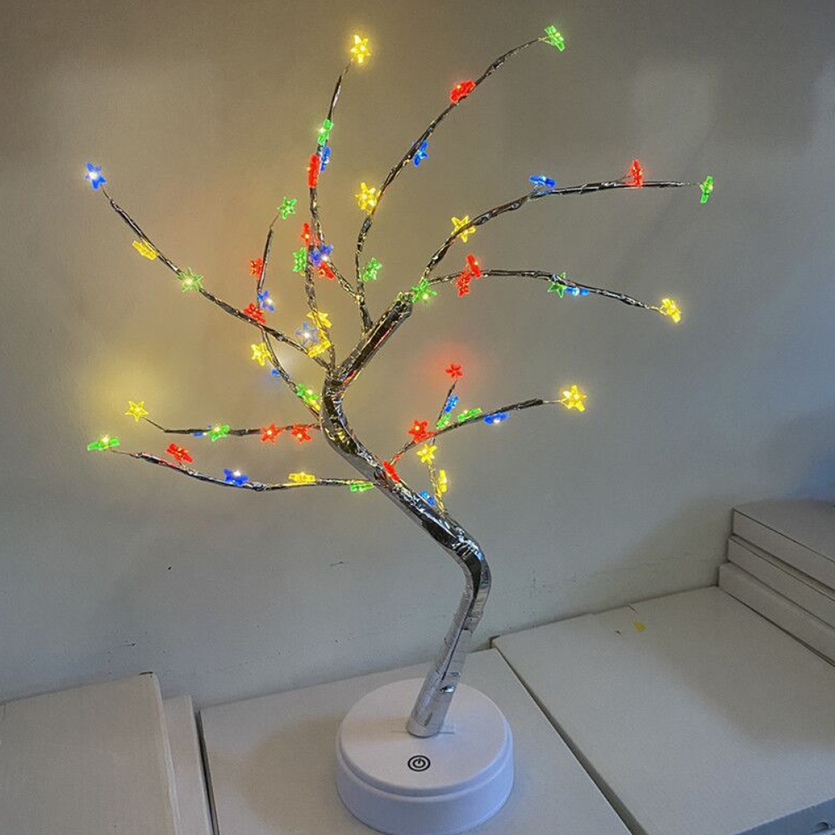 Ein dekorativer Baum mit bunten sternförmigen Lichtern auf weißer Oberfläche.