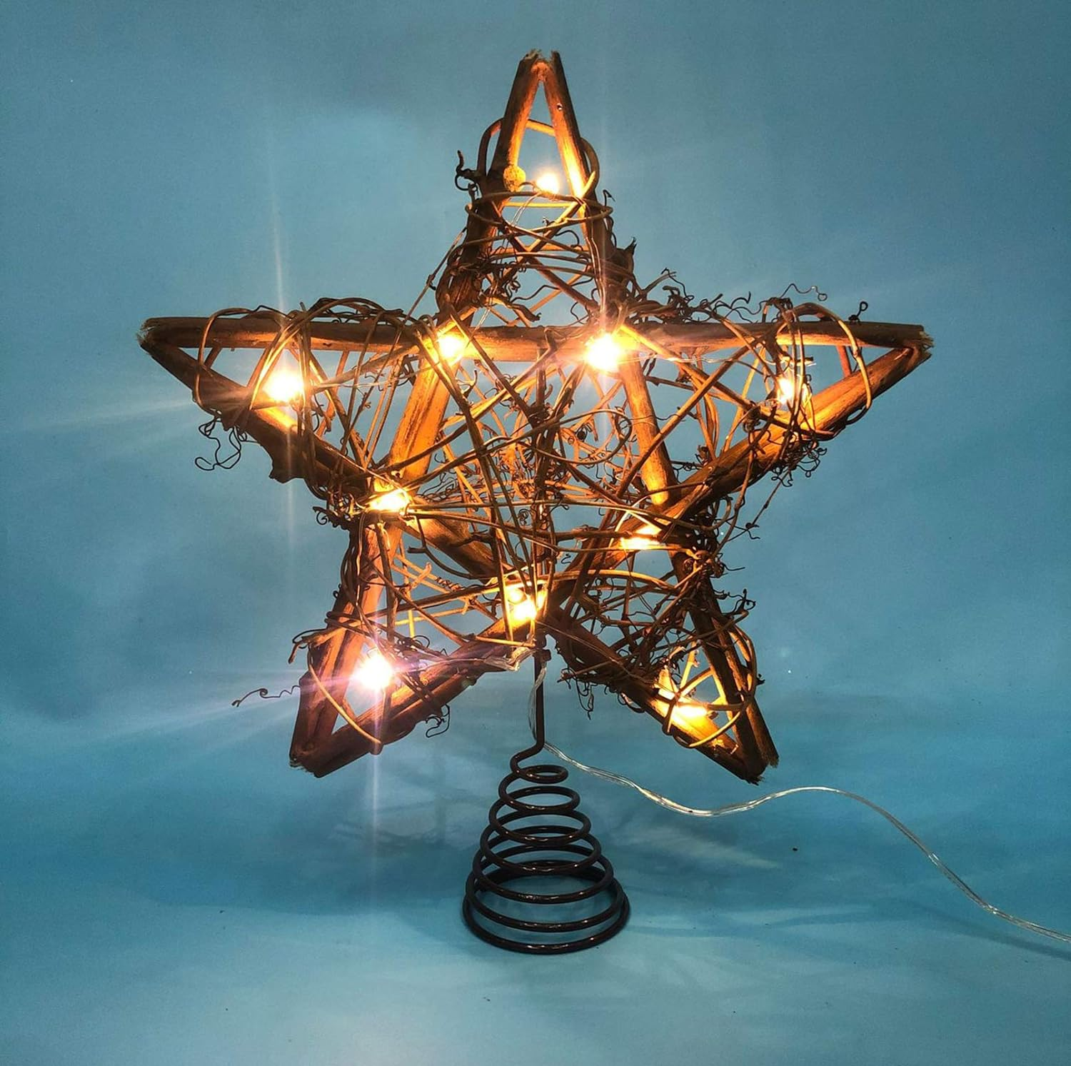 Sternförmige Weihnachtsbaumspitze aus geflochtenen braunen Stäben mit Lichtern auf blauem Hintergrund.