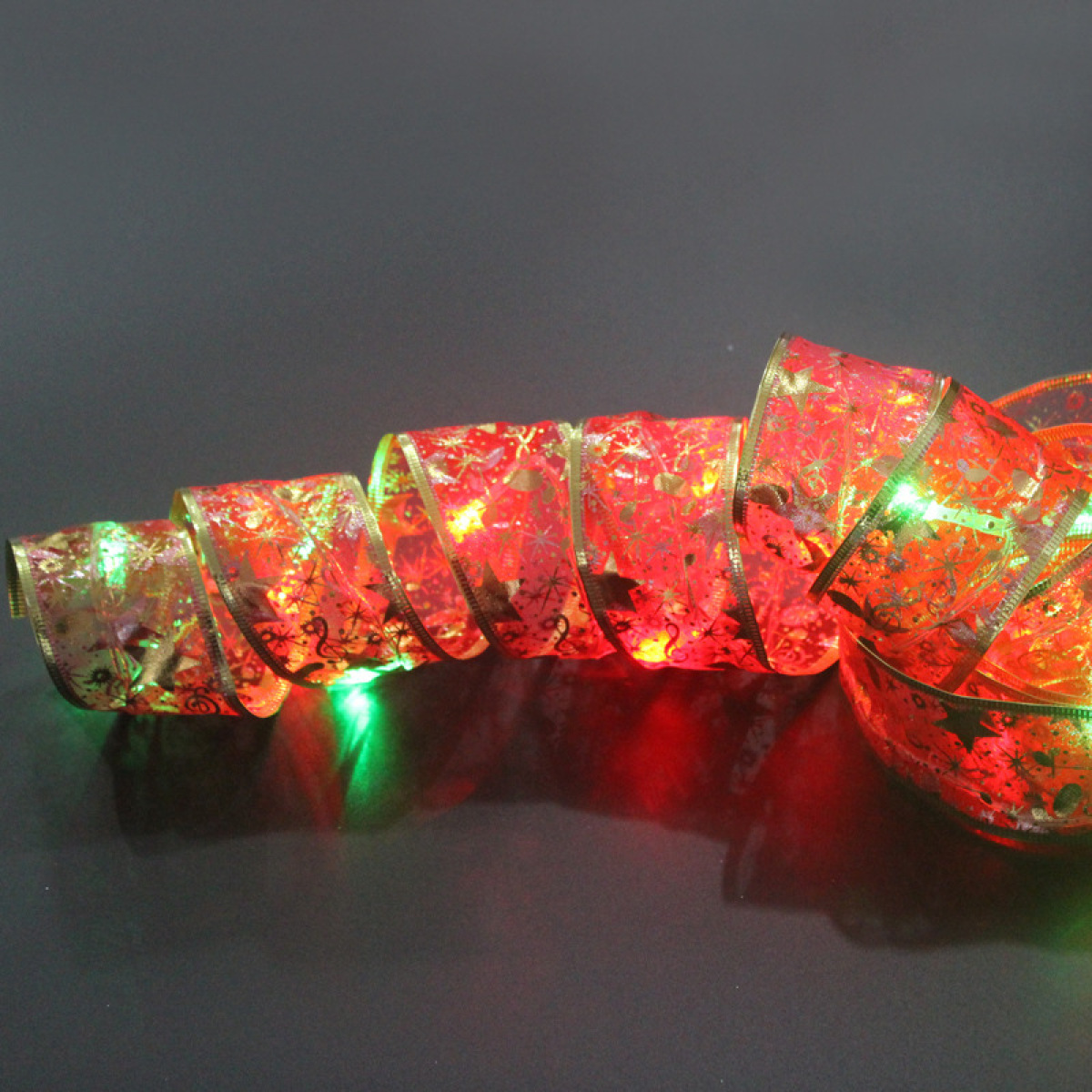 Eine aufgerollte, beleuchtete Schleife mit rotem Muster und grünen Lichtern auf dunklem Untergrund.