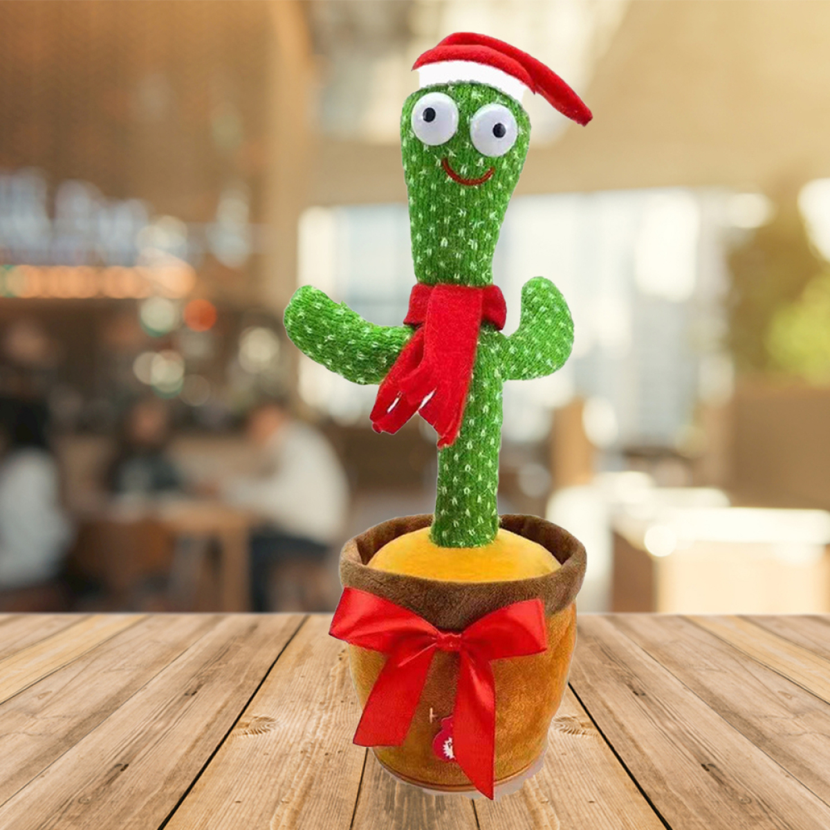 Ein Kaktus-Spielzeug in einem Topf, das einen Weihnachtsmannhut und einen Schal trägt. Der Hintergrund ist verschwommen.