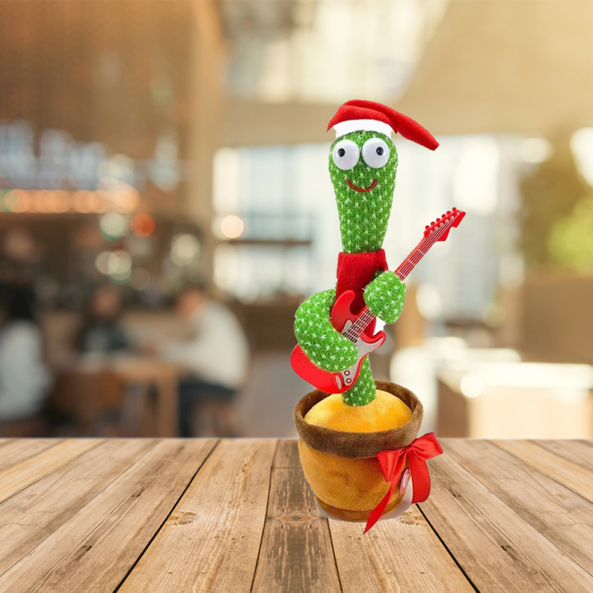 Singen Kaktus mit Weihnachtsmütze, Gitarre haltend, auf Holztisch stehend. Verschwommener Hintergrund.
