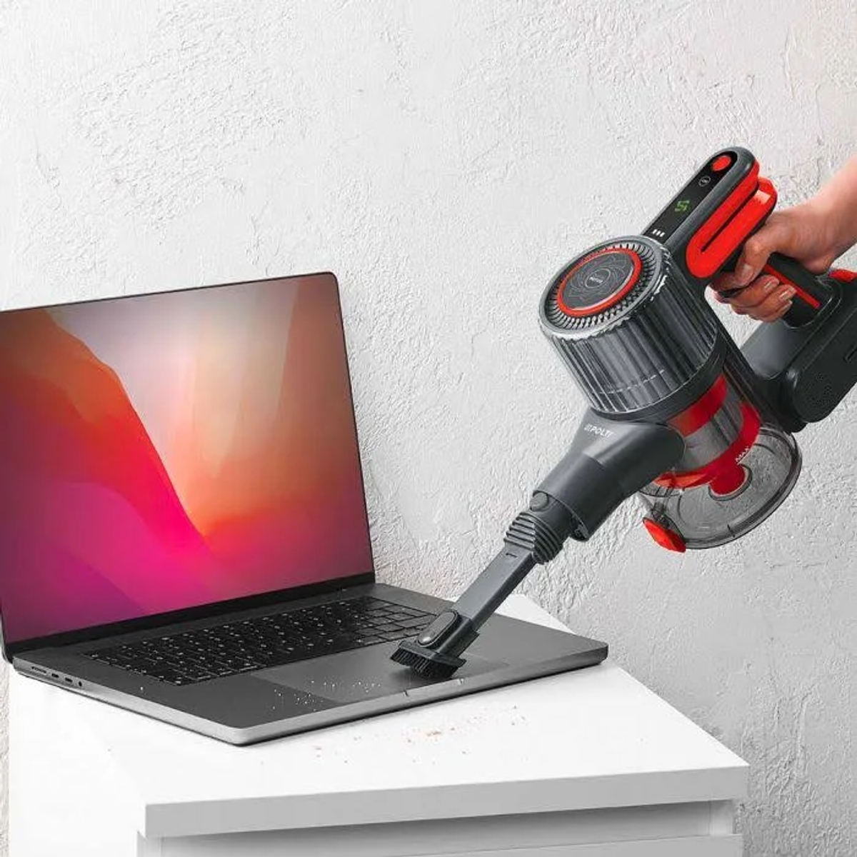 Una aspiradora limpiando una laptop en una mesa blanca.