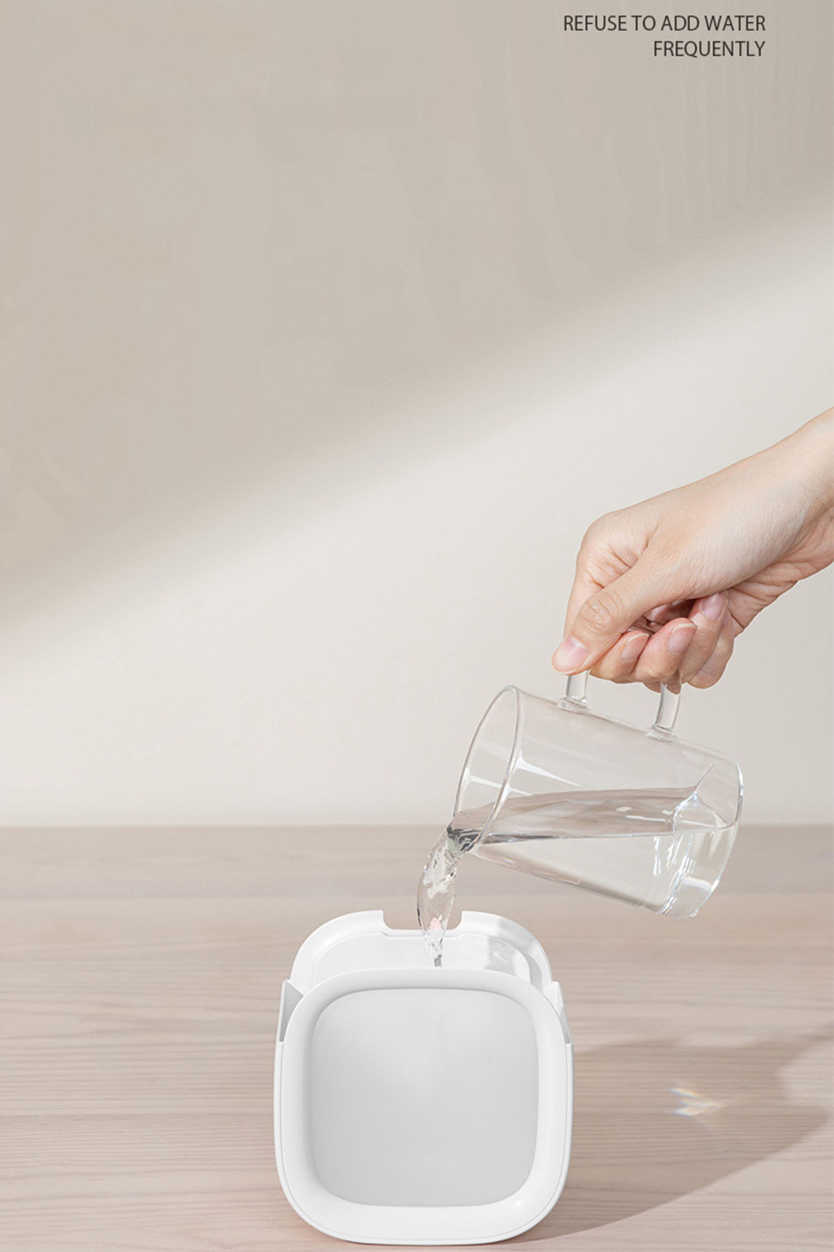 Eine Hand, die Wasser in einen weißen Behälter gießt. Text: Häufiges Hinzufügen von Wasser vermeiden.