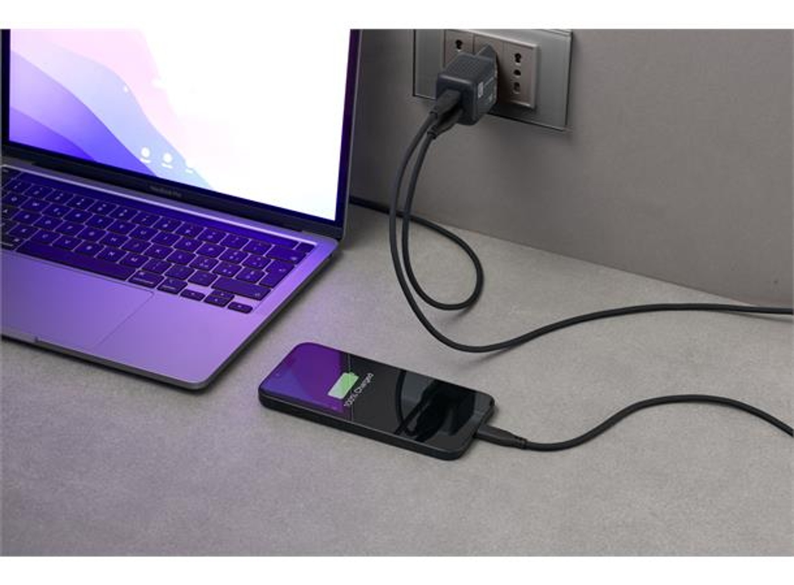 Laptop e telefono in carica. Il telefono mostra 100% carica. Caricabatterie collegato alla presa a muro.