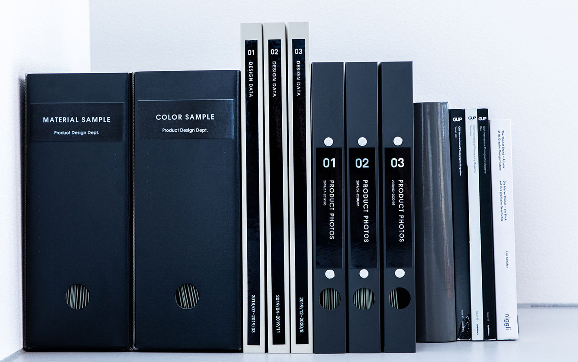Bücher und Akten in einer Reihe auf einem Regal. Schwarze Buchrücken mit weißen Etiketten.