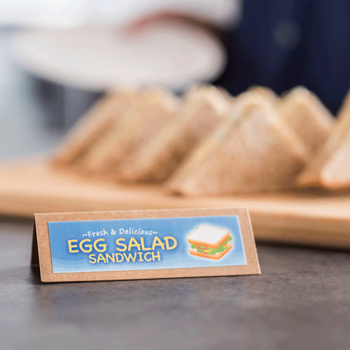 Ein Schild für ein Eiersalat-Sandwich mit Sandwiches auf einem Holzbrett.