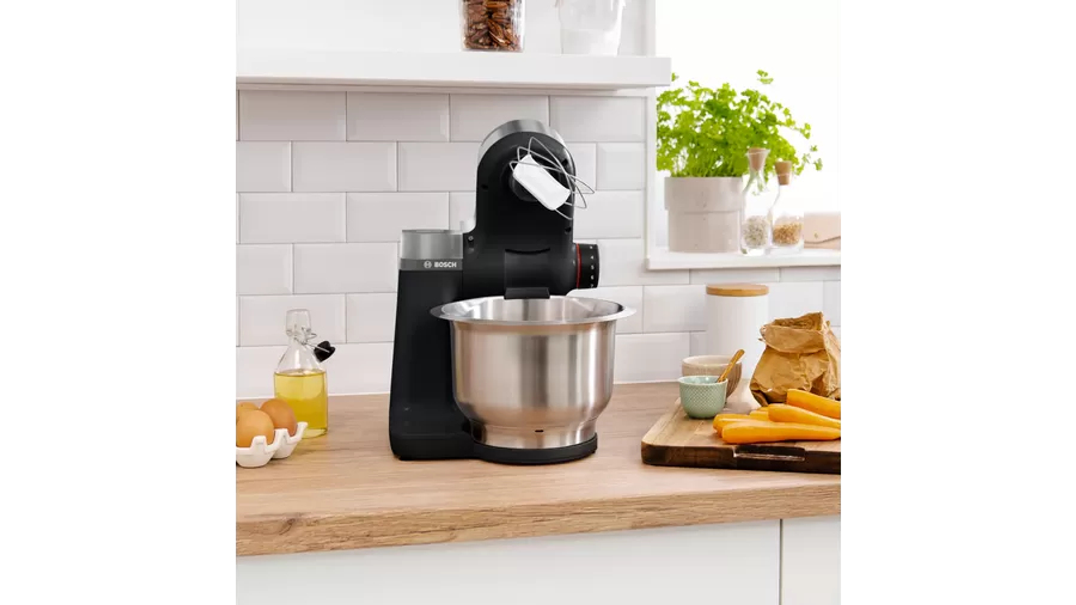 Batidora de cocina negra sobre una encimera de madera con ingredientes. Texto: Bosch.