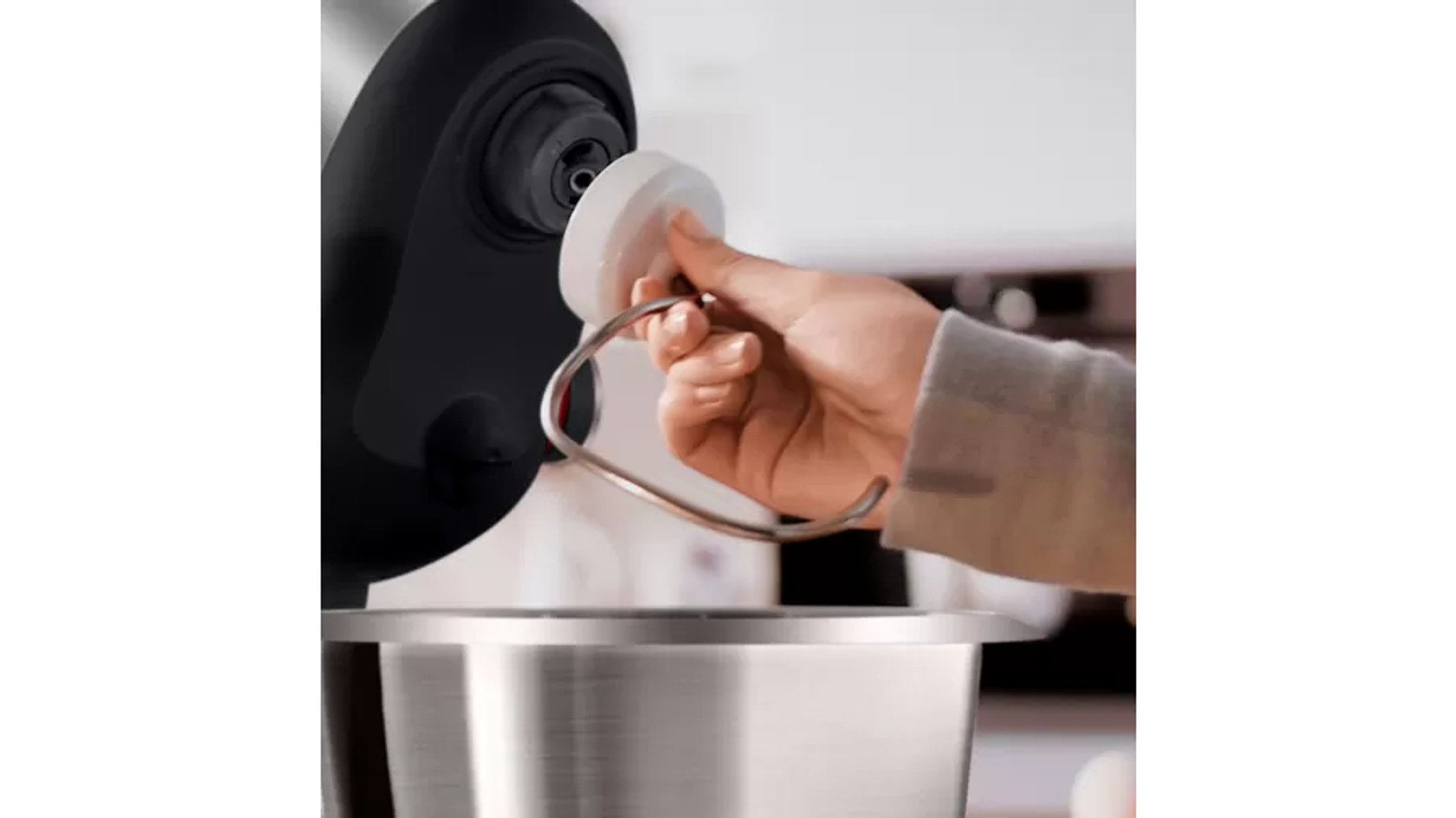 Una mano quitando el gancho de un cuenco mezclador, parte de un electrodoméstico de cocina negro.
