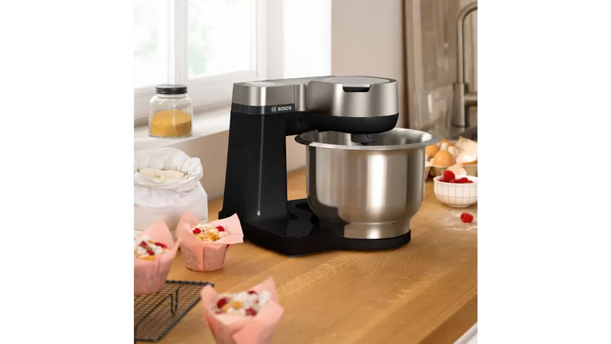 Una cocina con una batidora de pie negra y plateada, cupcakes e ingredientes sobre una encimera de madera.