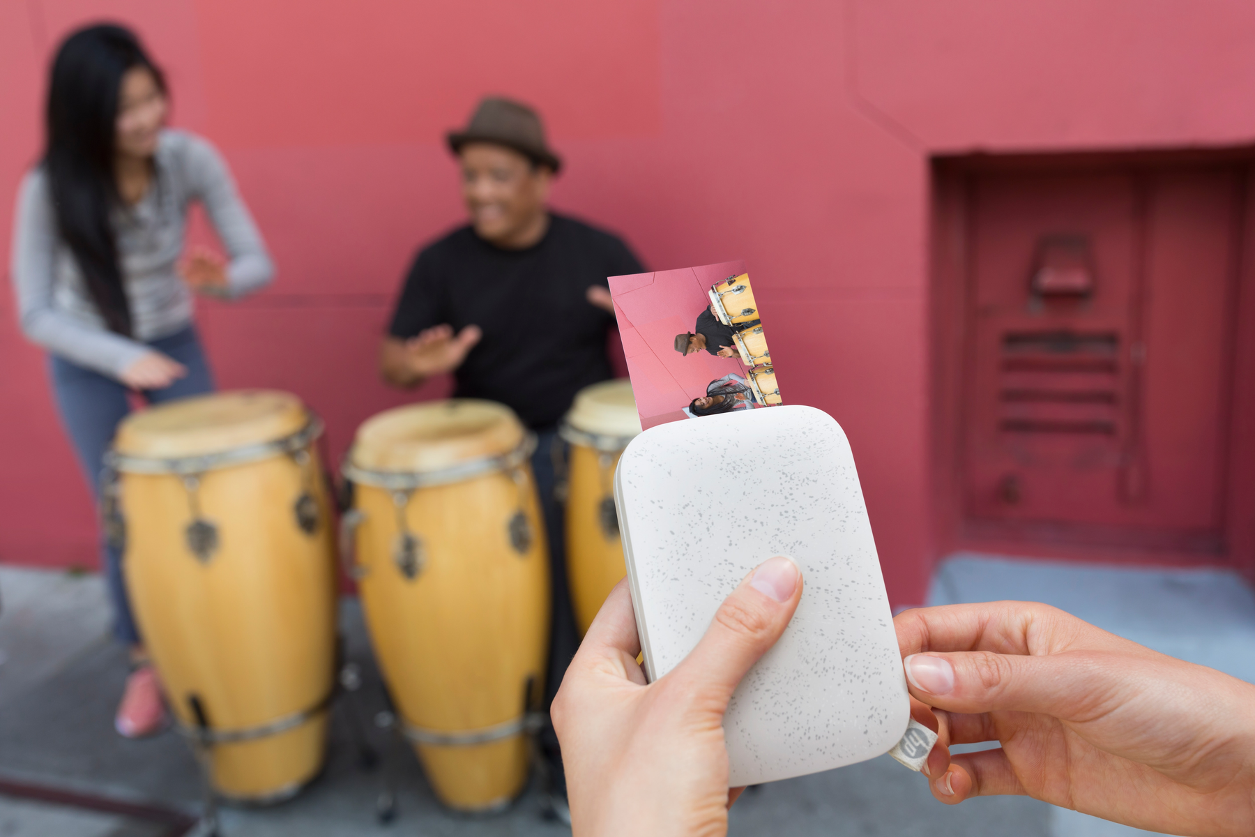 Ludzie z bębnami. Jedna osoba drukuje zdjęcie z białej drukarki. Czerwone tło.
