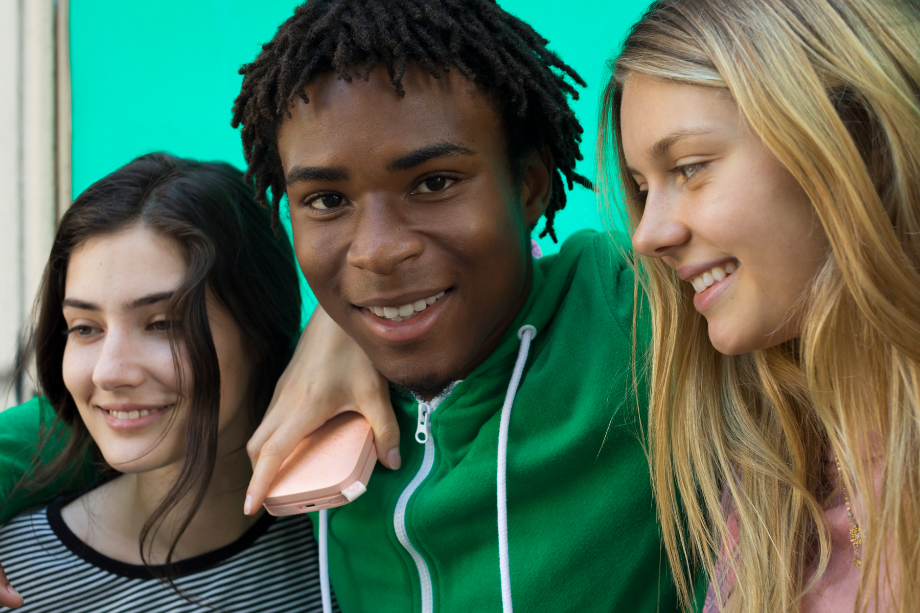 Trzy uśmiechnięte młode osoby, jedna z telefonem.