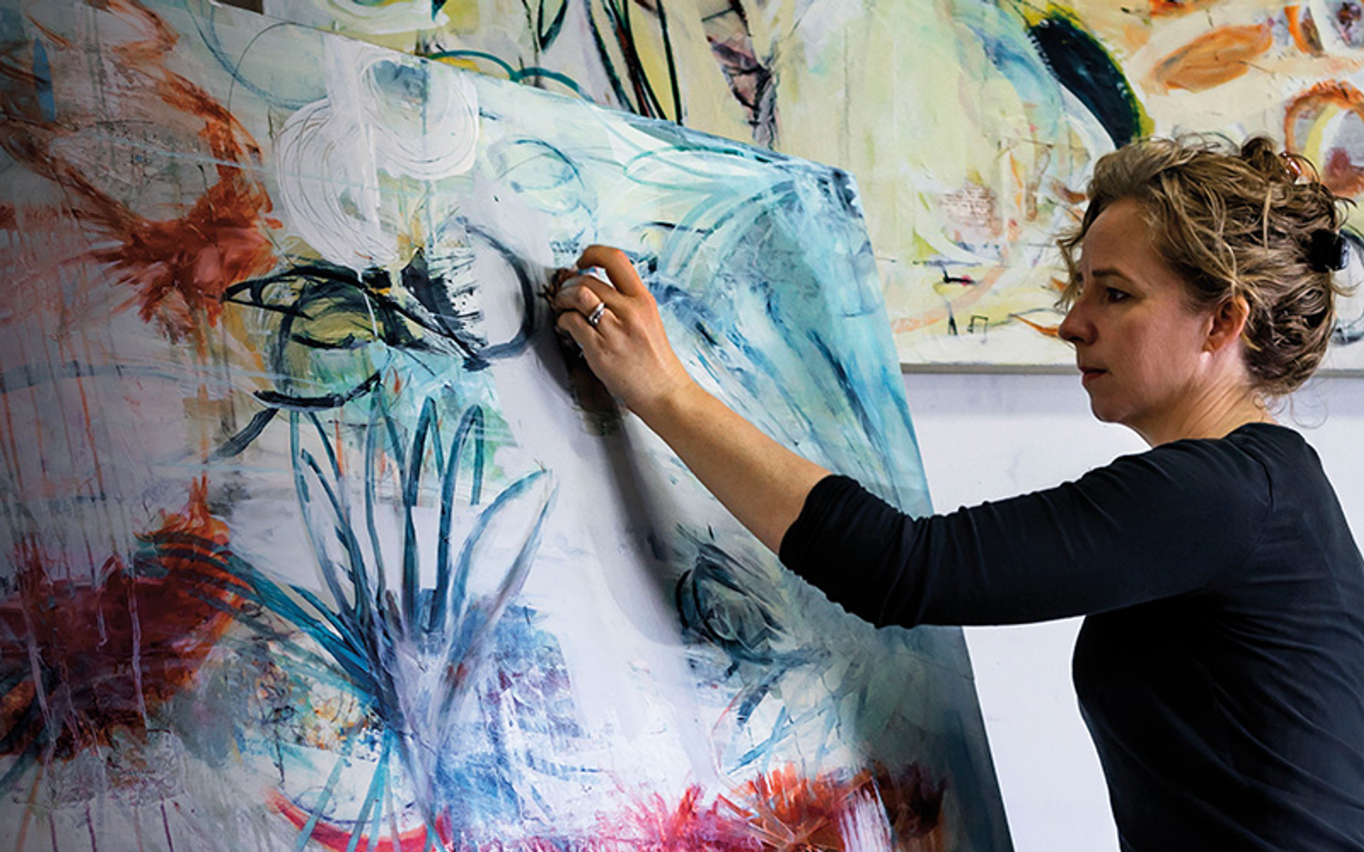 Kobieta w czarnej koszuli maluje na dużym abstrakcyjnym płótnie.