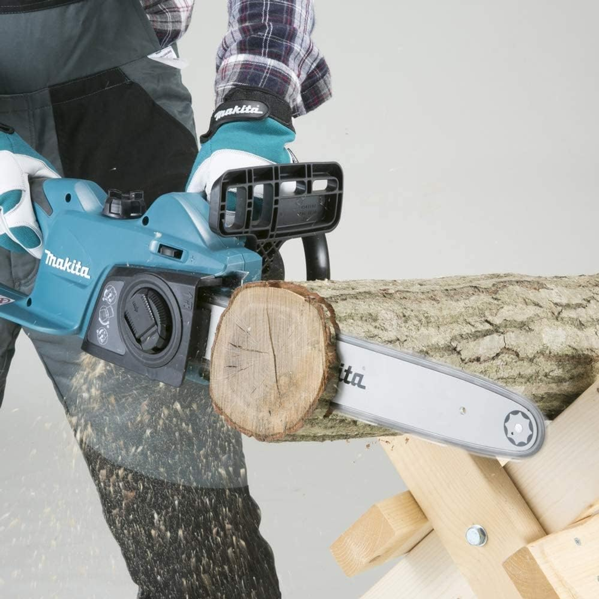 Eine Person, die eine blaue Makita-Kettensäge benutzt, um einen Baumstamm auf einem hölzernen Sägebock zu schneiden.