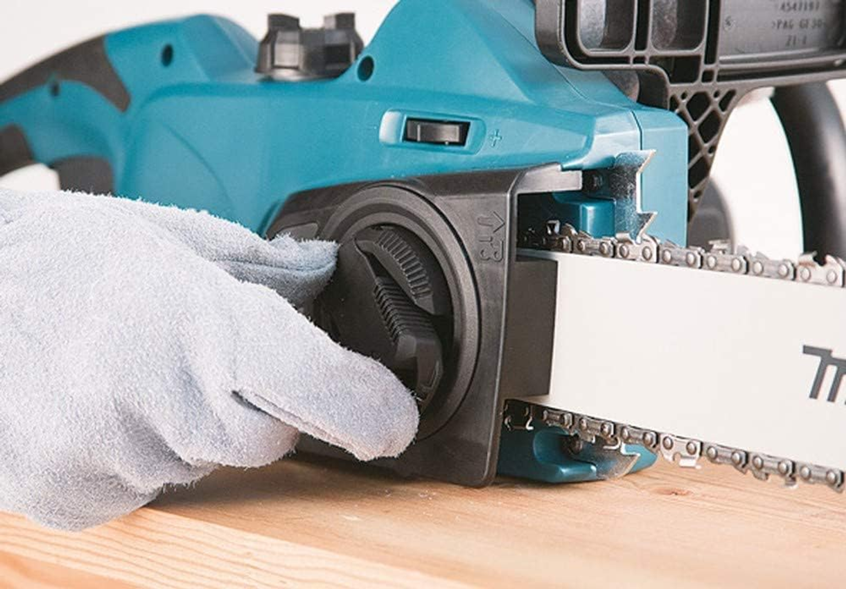 Hand im Handschuh, die eine türkisfarbene Kettensäge auf Holz einstellt.