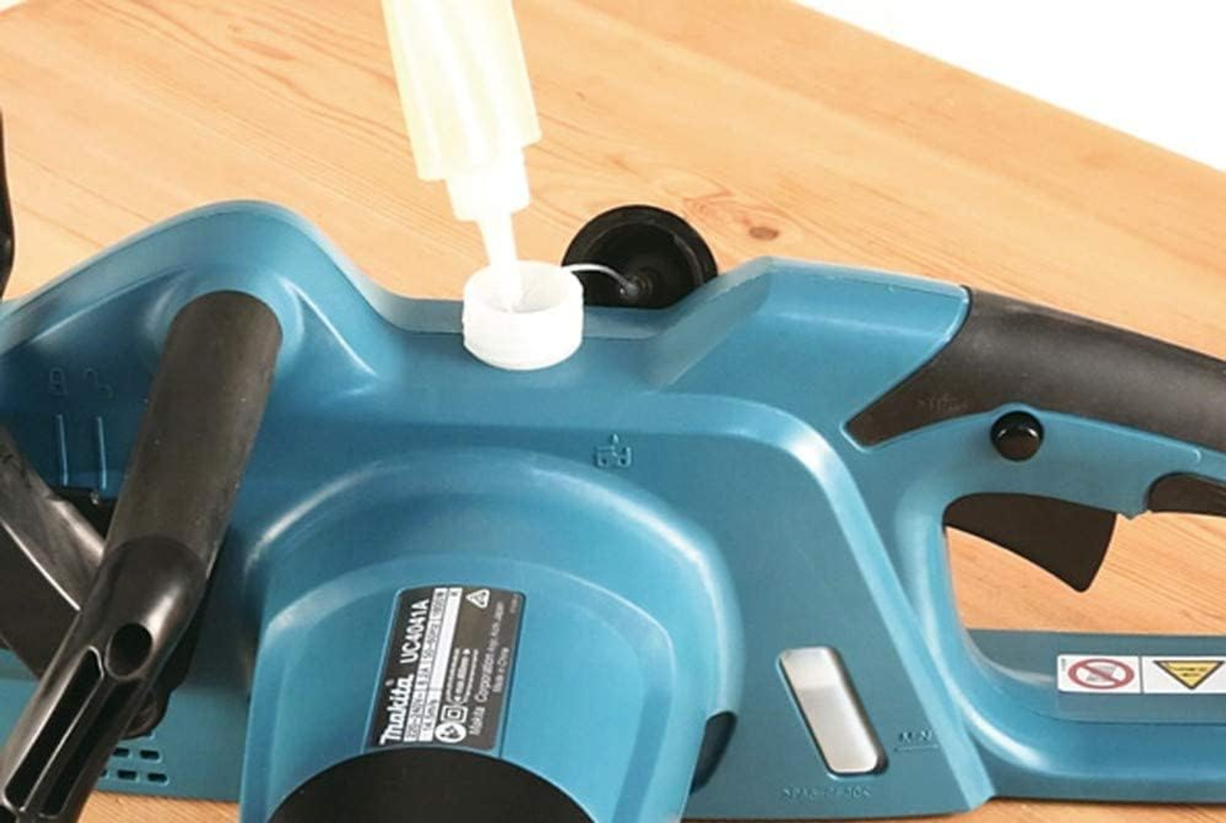 Eine Kettensäge mit einer Flasche, die Öl hineingießt. Die Maschine ist blau und schwarz.