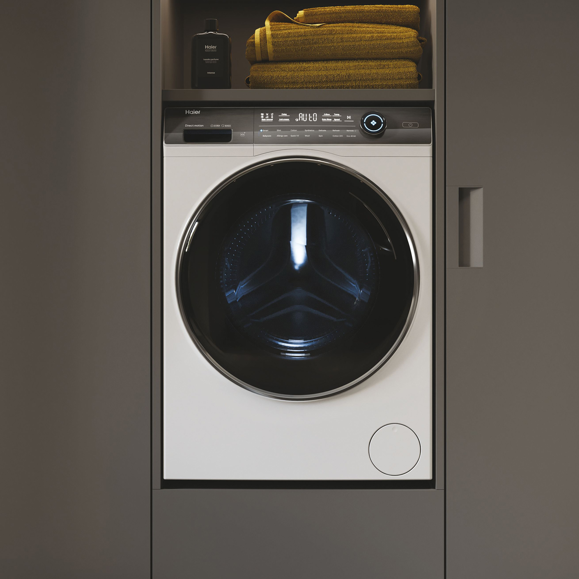 Weiße Waschmaschine in einem Schrank eingebaut, mit Handtüchern und dunklem Hintergrund.