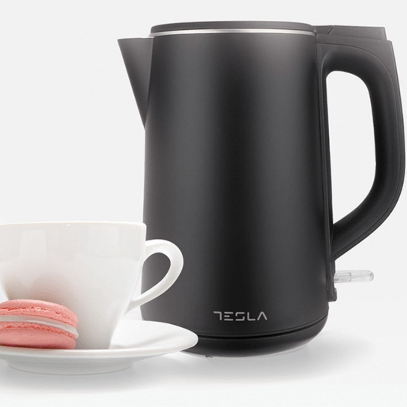 Hervidor eléctrico negro con taza blanca y macaron rosa. El hervidor tiene un cuerpo negro y un asa.