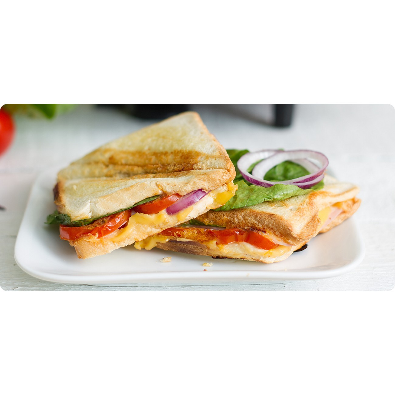 Dwie tosty na białym talerzu, z sałatą i pomidorem.