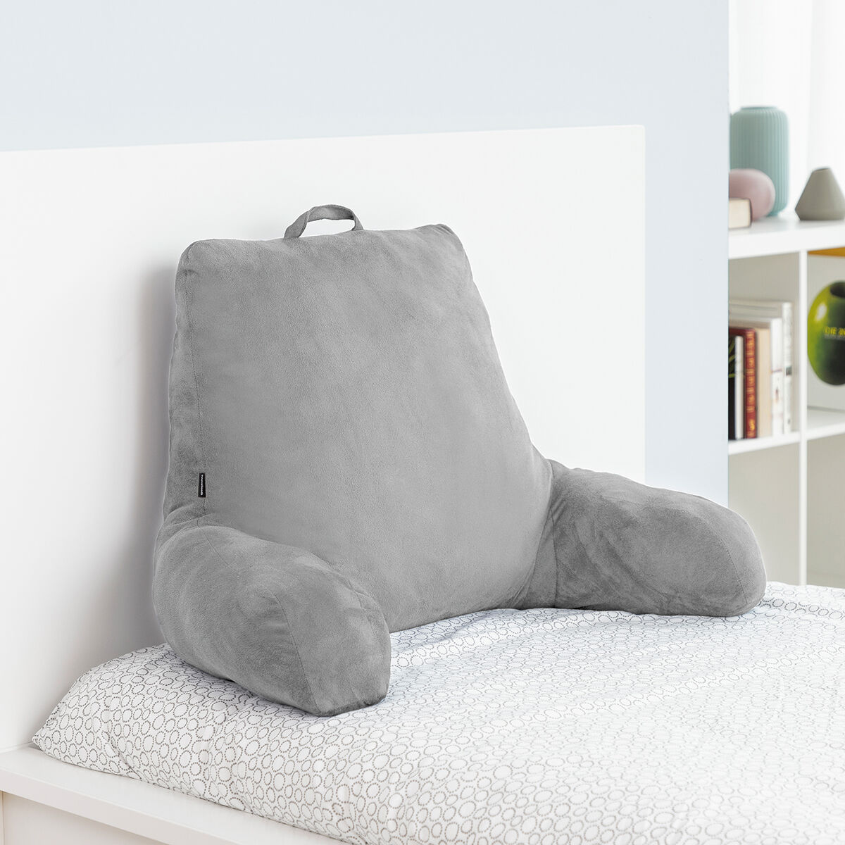 Graues Bettkissen auf einem Bett mit gemusterten Laken. Weißer Wandhintergrund.