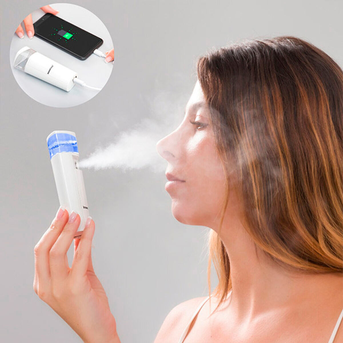 Una donna usa un vaporizzatore facciale portatile, con un telefono in carica sullo sfondo.