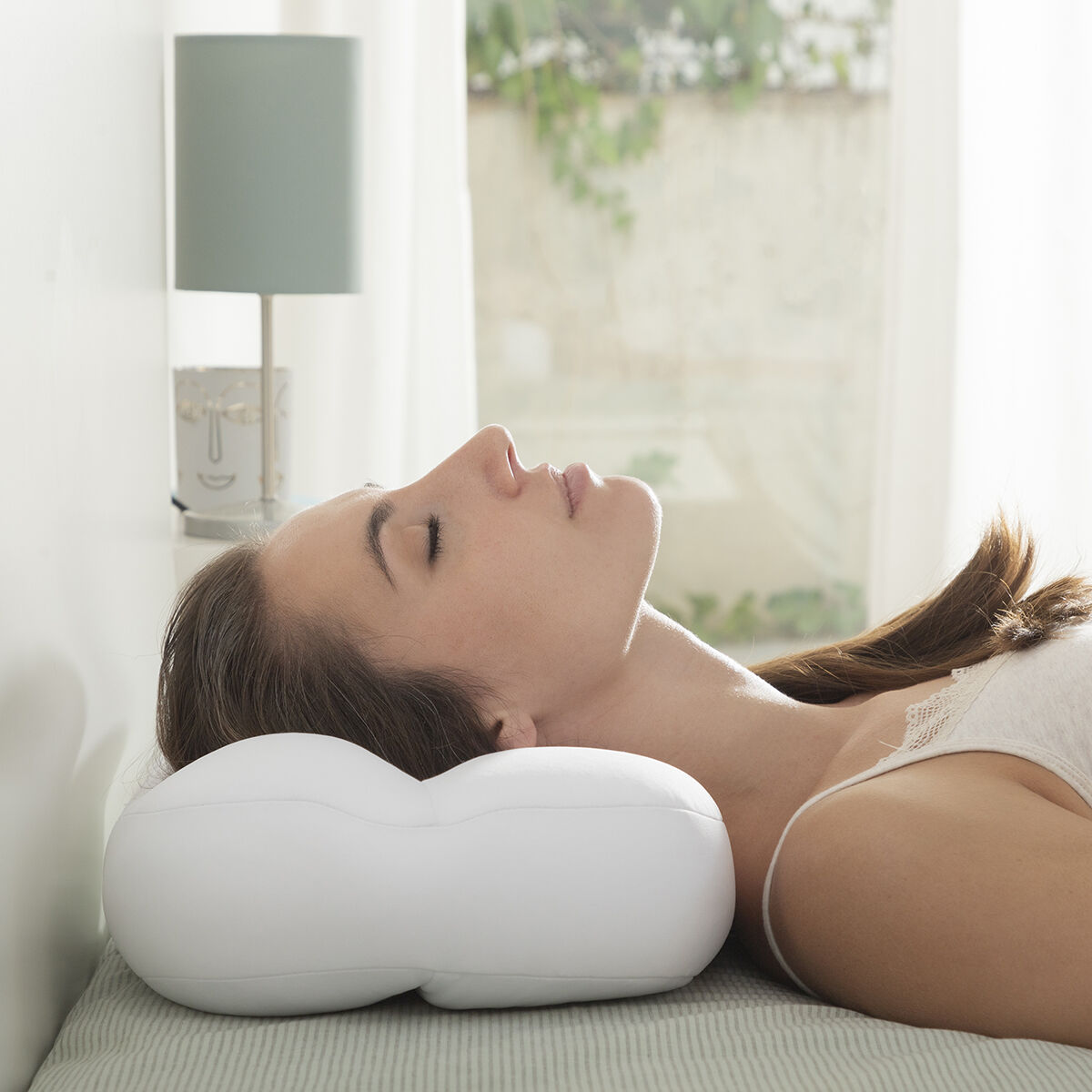 Una donna con gli occhi chiusi riposa su un cuscino bianco a letto.