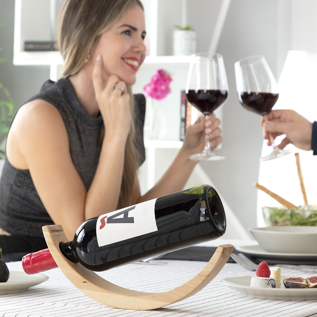 Donna e uomo brindano con calici di vino. Bottiglia di vino su un supporto di legno.