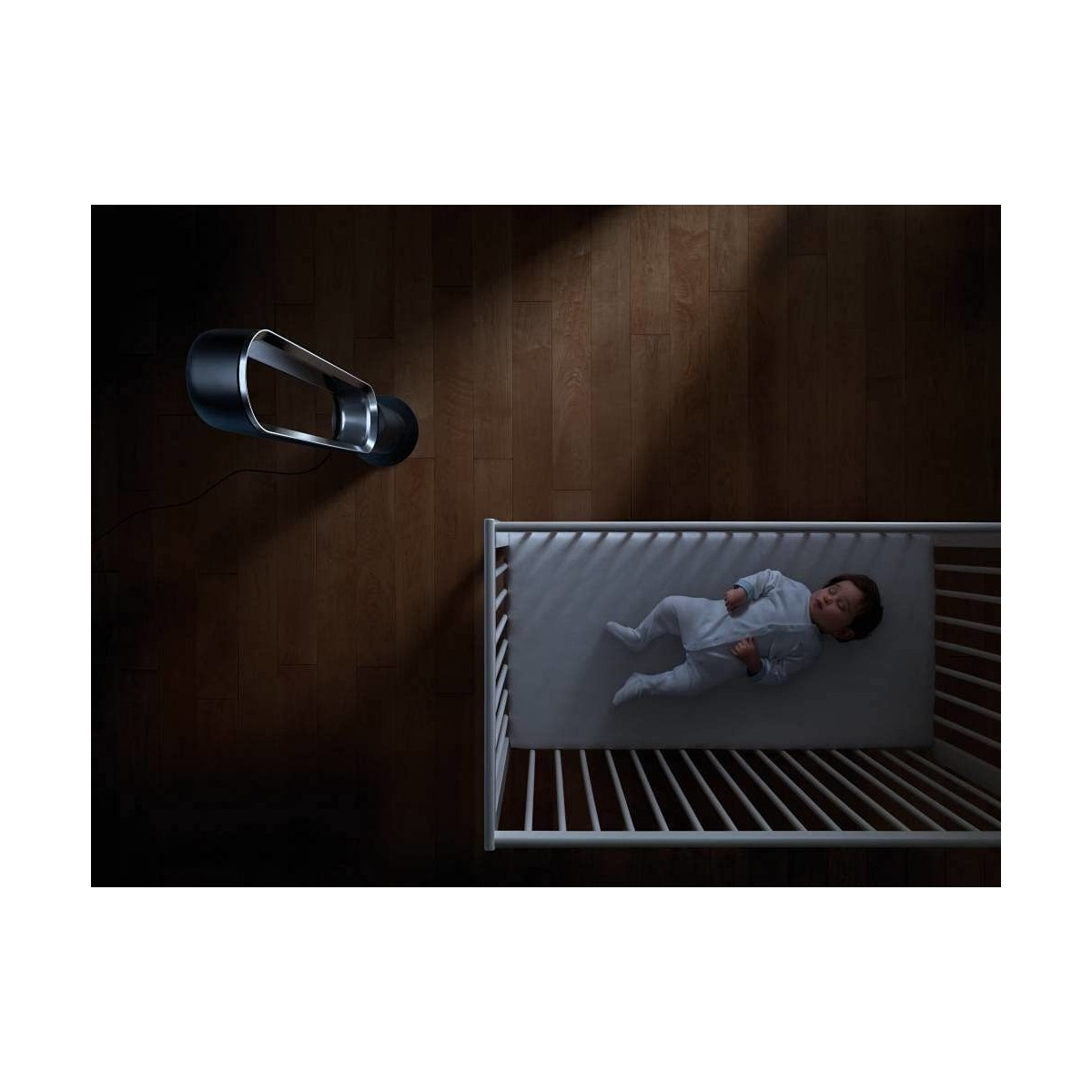 Ein Baby schläft in einem Kinderbett mit einem Ventilator darüber. Holzboden im Hintergrund.