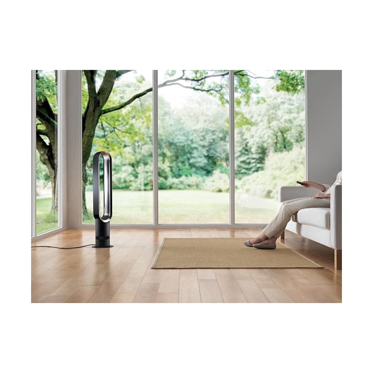 Eine Person sitzt auf einem weißen Sofa mit einem Ventilator und einem Teppich in einem hellen Raum mit Aussicht.