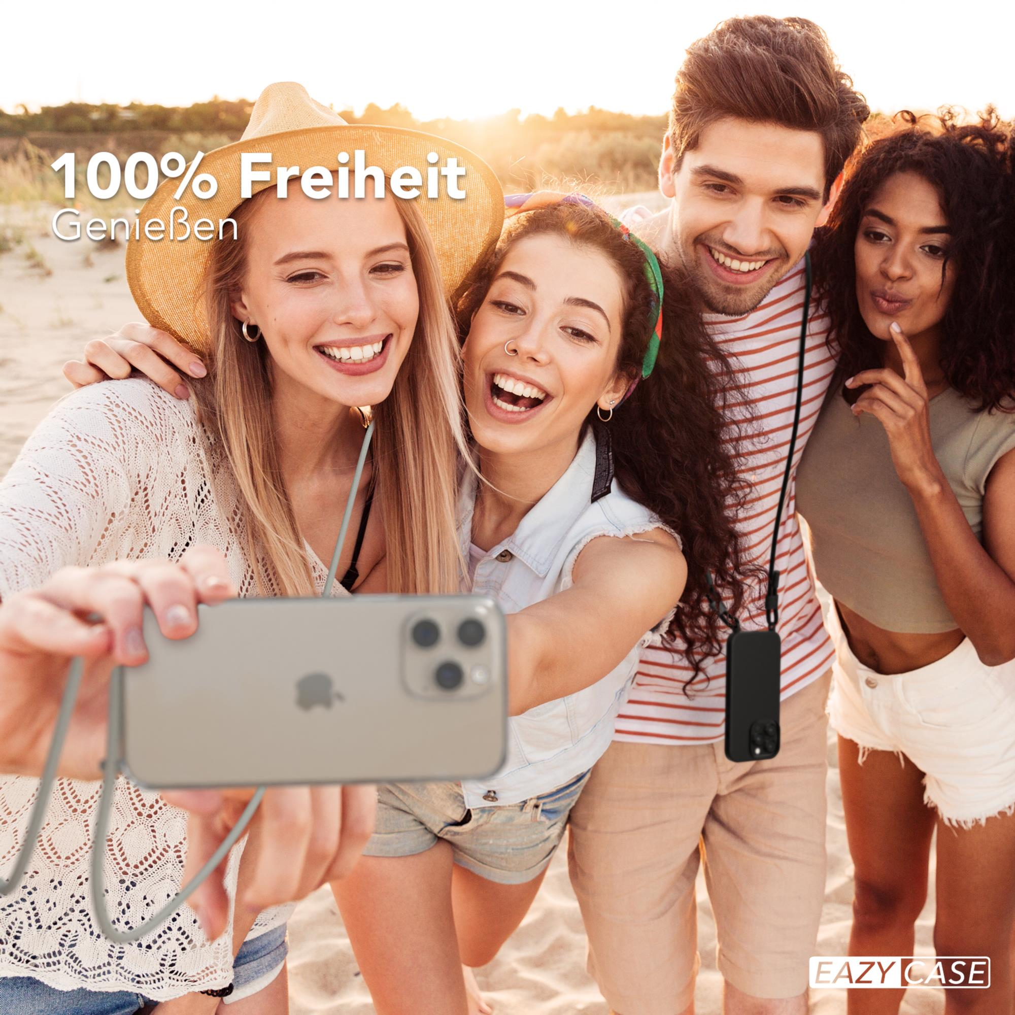 Vier lächelnde Personen machen ein Selfie am Strand, halten ein Telefon an einer Schnur.