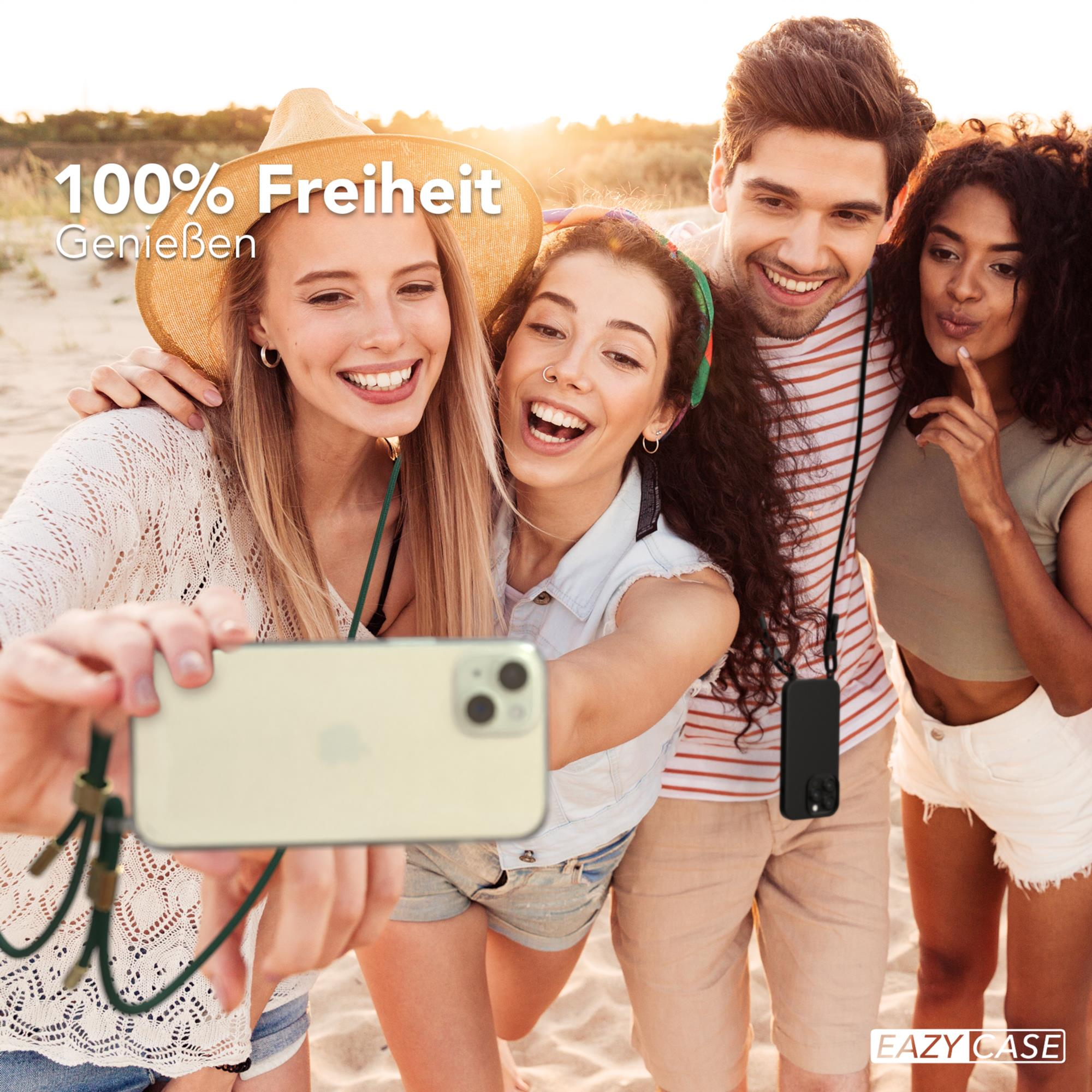 Vier Personen machen ein Selfie. Frau hält Telefon mit grünem Band. Strandhintergrund, glückliche Gesichter.